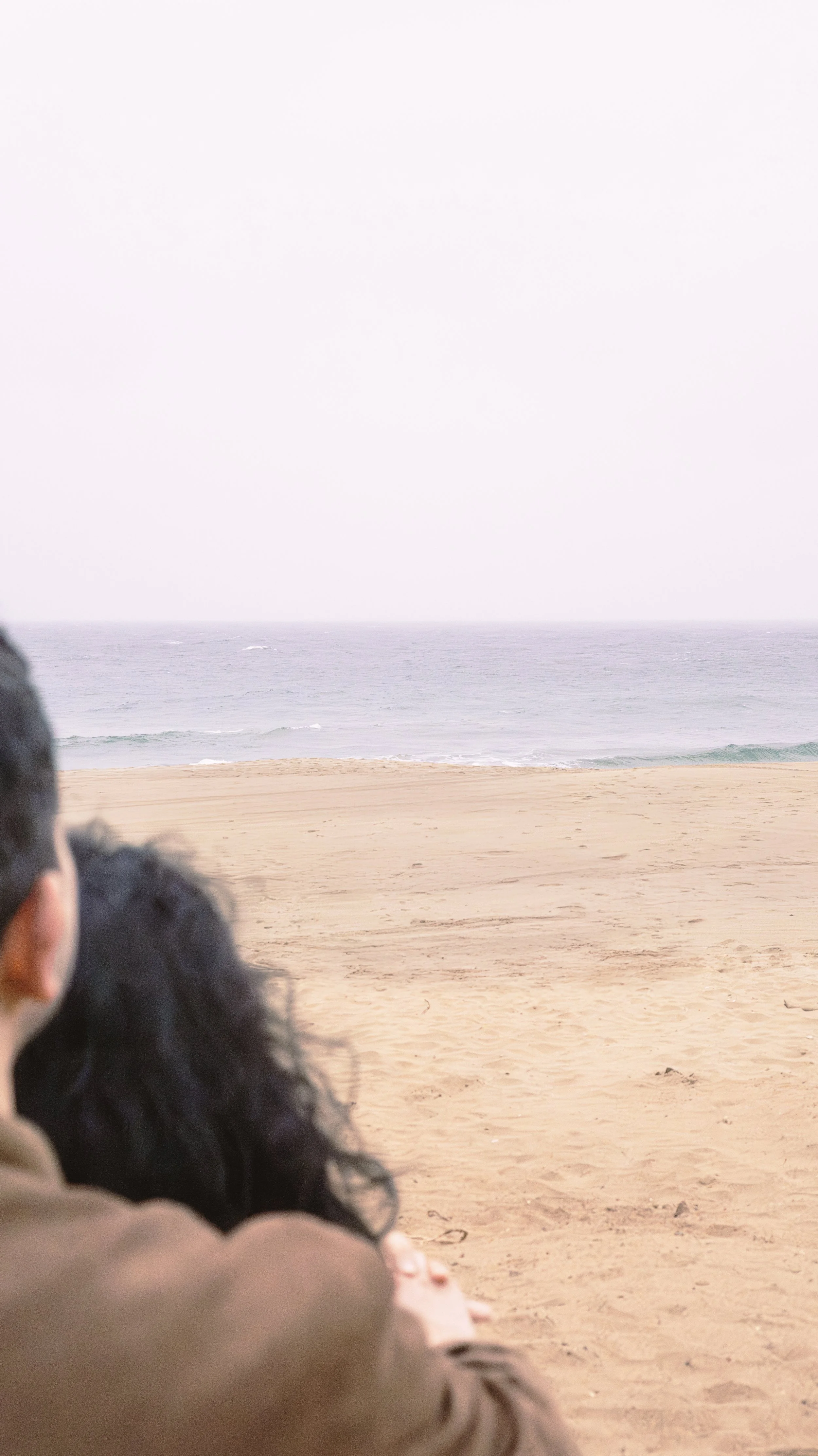 View of a beach with sand, the ocean, and sky in the background, with some people in the foreground.