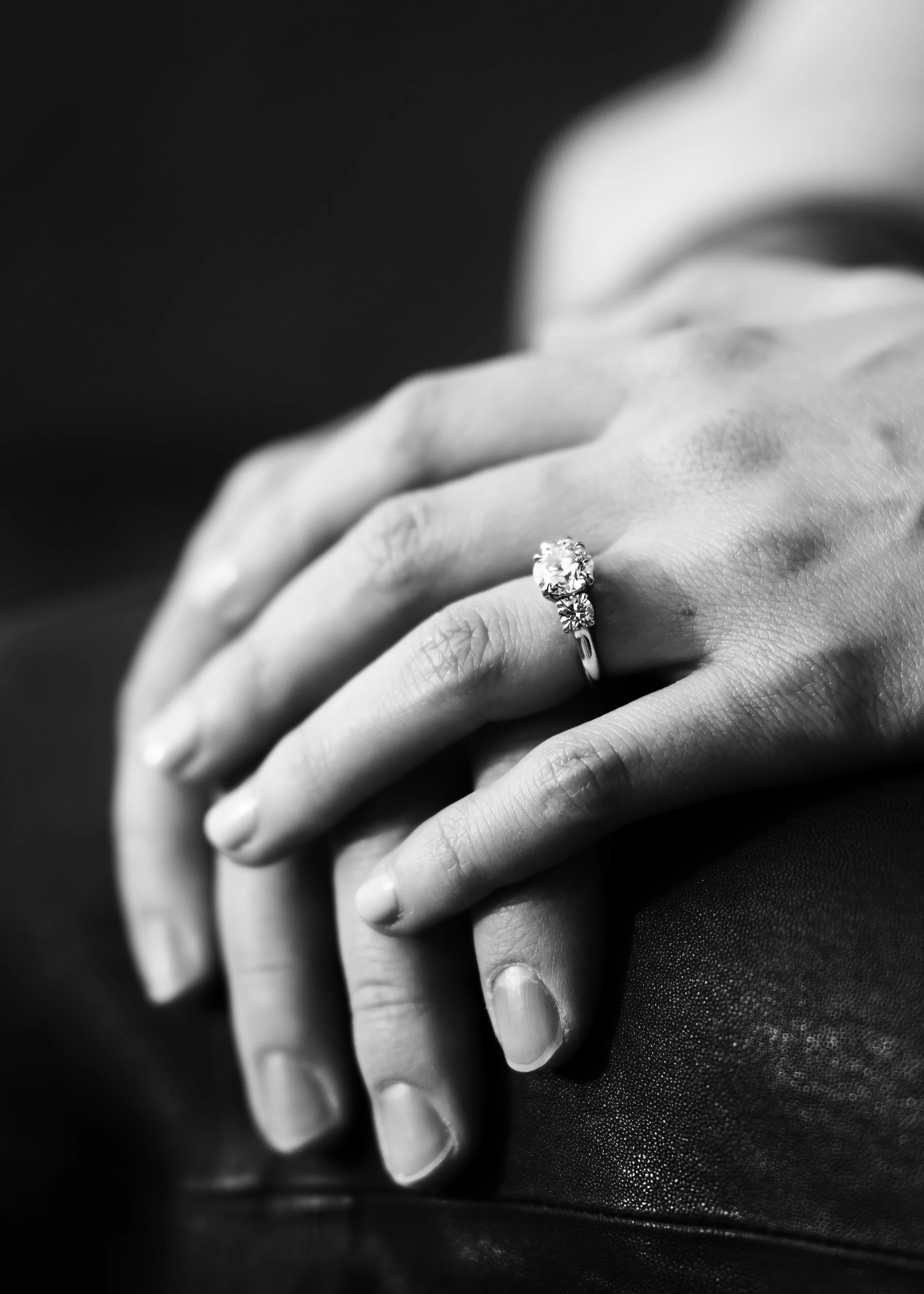 Close-up black and white photograph of hands with one hand wearing an engagement ring with a large diamond.