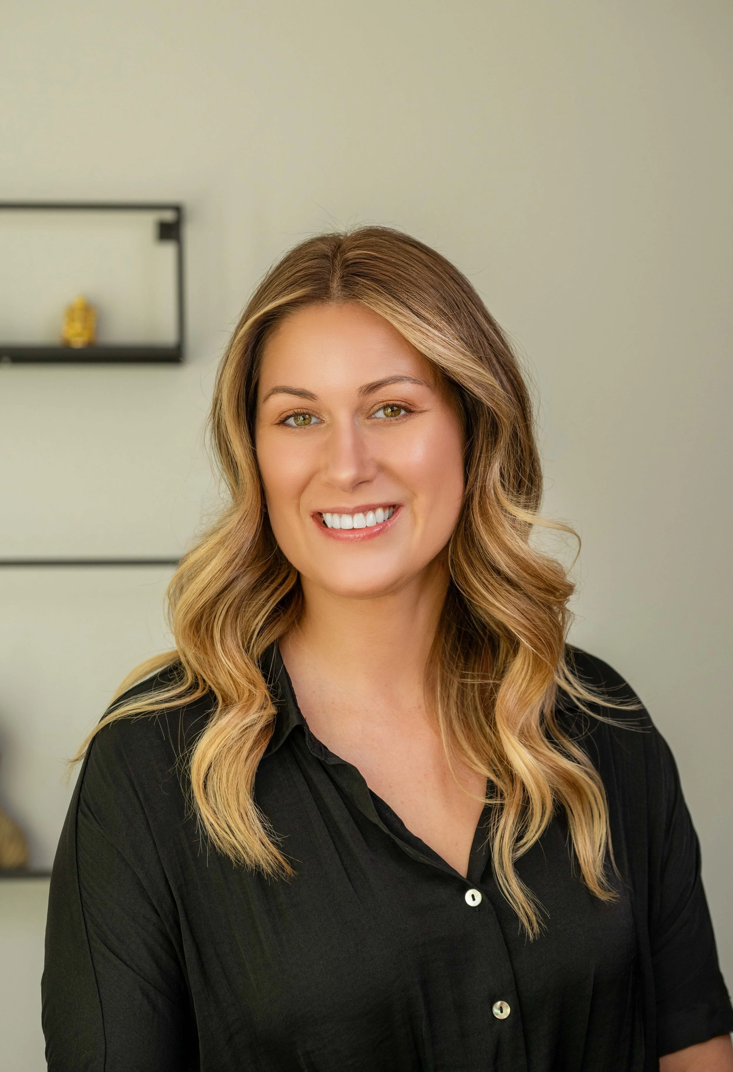 A woman with long blond hair styled in loose waves, smiling and wearing a black button-up shirt.