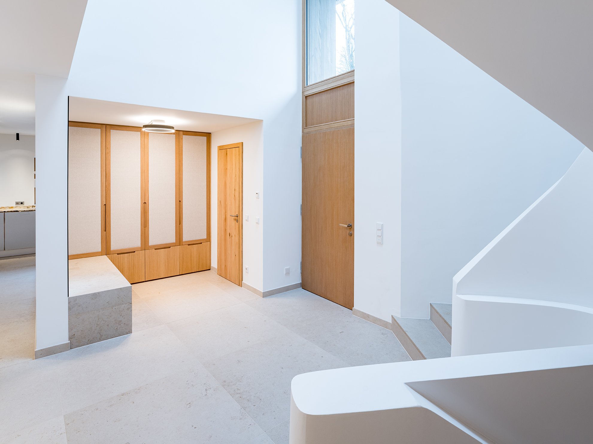 Moderner Eingangsbereich mit weißen Wänden, Holztüren und Treppe, viel natürliches Licht.