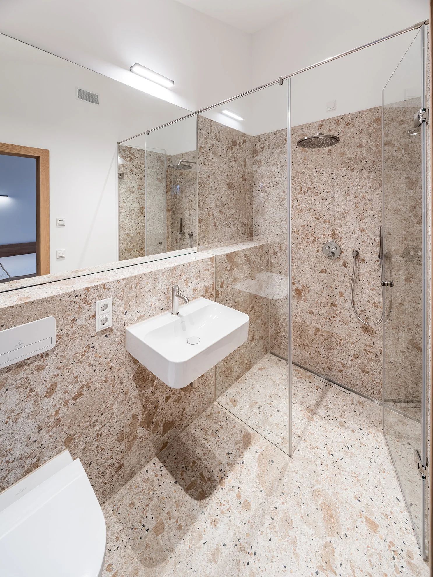 Modernes Badezimmer mit Natursteinfliesen, Dusche mit Glasabtrennung, kleiner weißer Wandwaschbecken und Spiegel