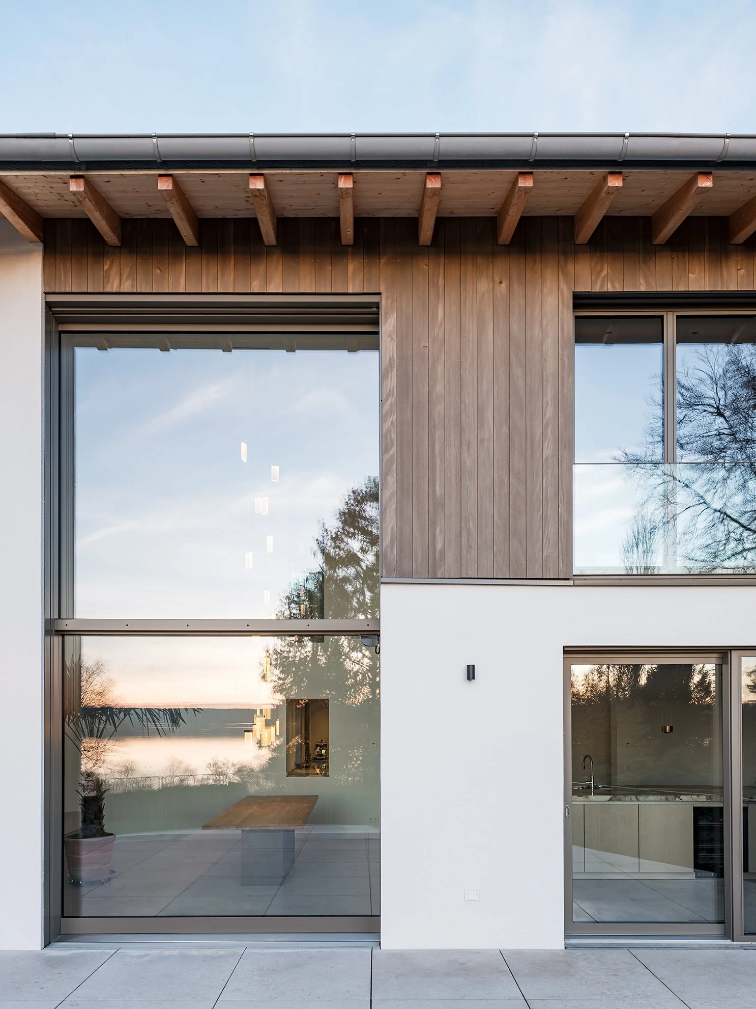 Modernes Haus mit großen Fenstern, teilweise aus Holz und teilweise weiß gestrichen, bei Sonnenuntergang