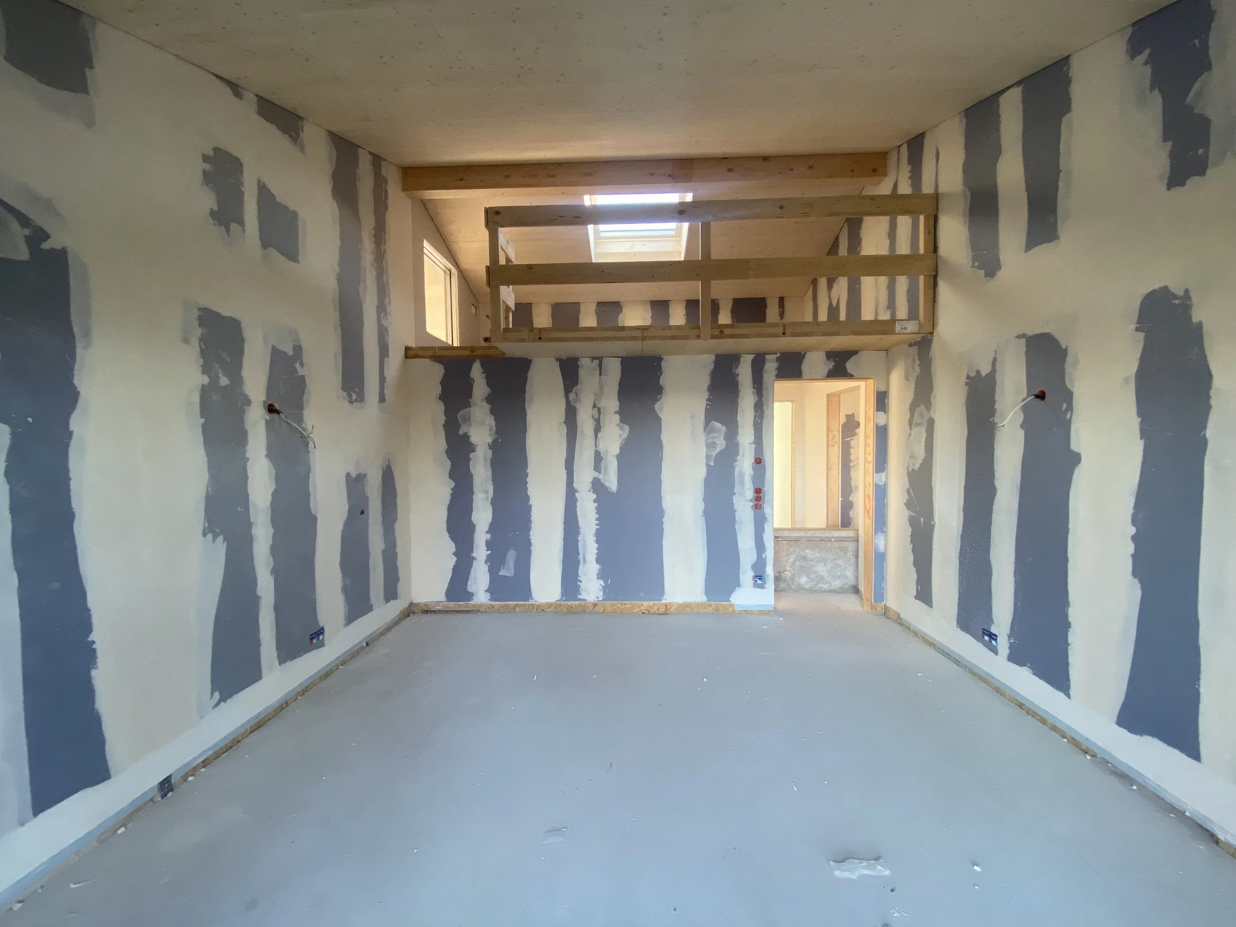 Innenansicht eines im Bau befindlichen Zimmers mit unstreichen Wänden, einer Zwischendecke und einem Holzabsatz.