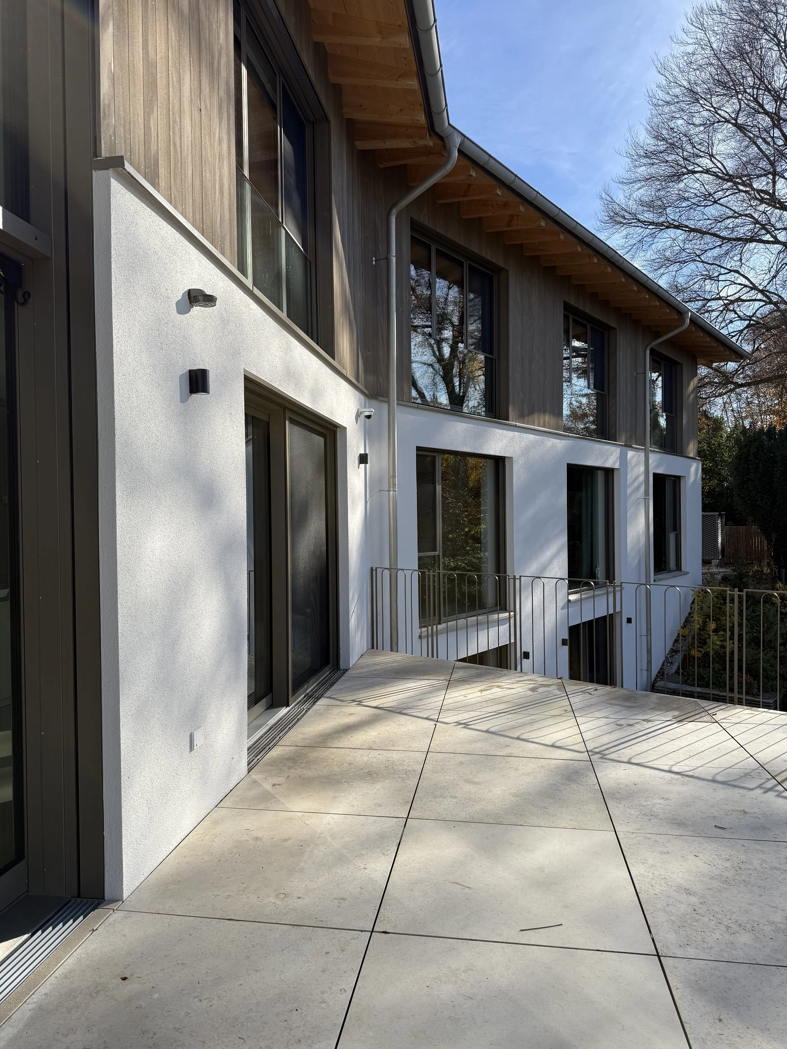Moderner mehrstöckiger Wohnkomplex mit Holz- und Putzfassade und großem Balkon, Blick auf einen Patio und eine Terrasse.