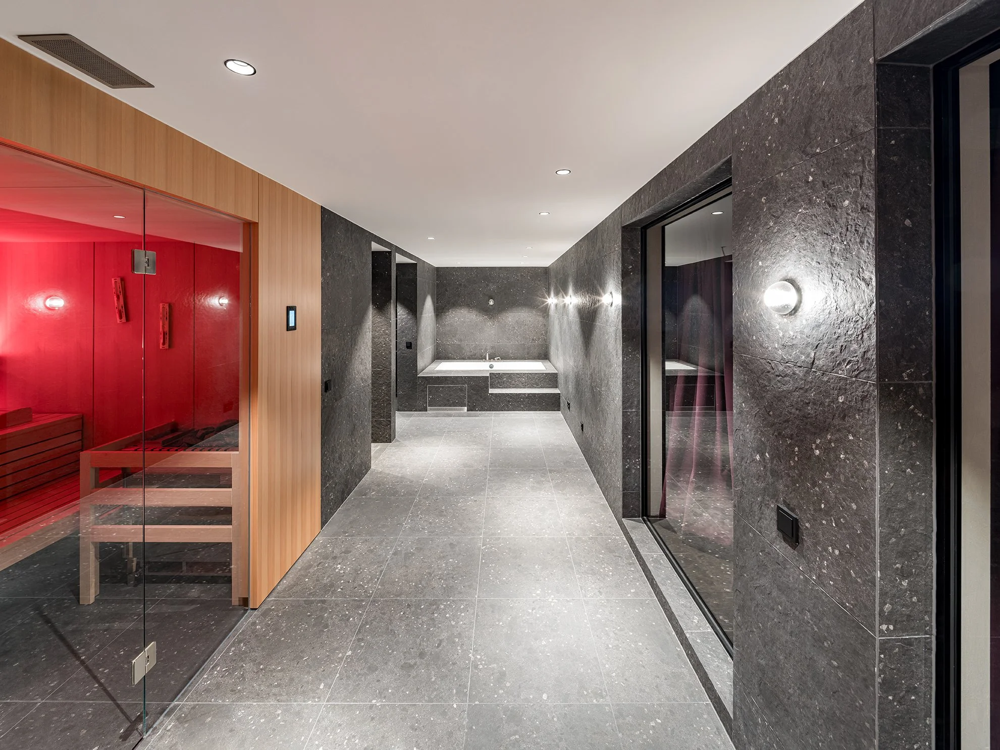 Moderner, eleganter Wellnessbereich mit Sauna, Massagebadewanne und Ruheraum, gepolsterte Sitze, dunkle und helle Fliesen, sanfte Beleuchtung