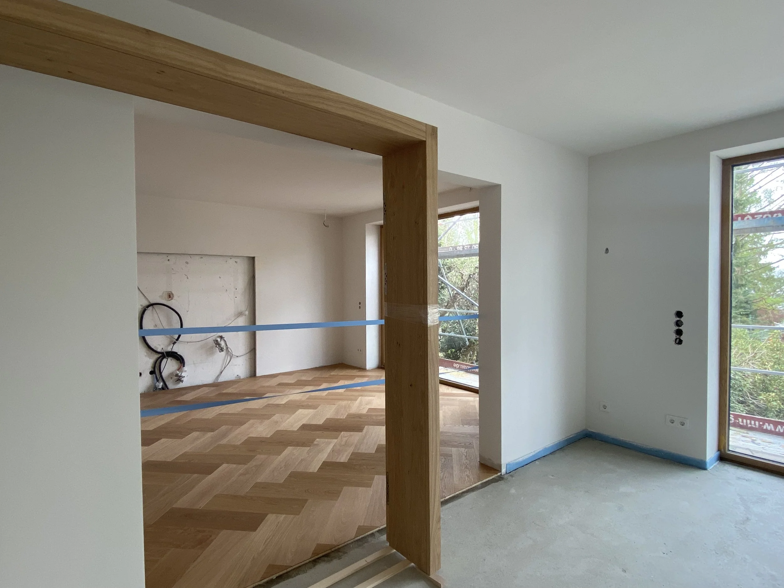 Innenraum eines Hauses im Bau, mit unvollendeten Wänden, Fenstern und einem Holzfußboden im Flur