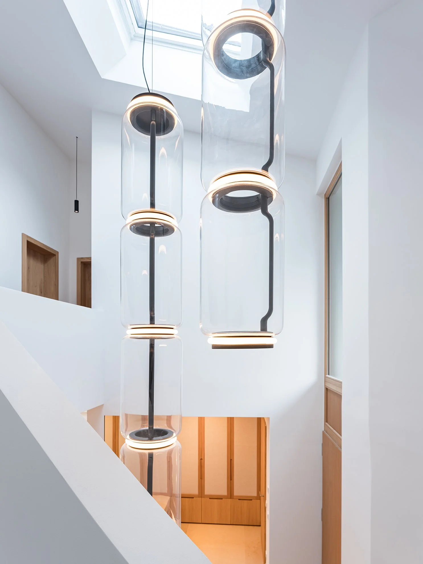 Moderne Hängelampen in einer weißen, minimalistischen Innenraumgestaltung, mit Holzdetails und einem Dachfenster.