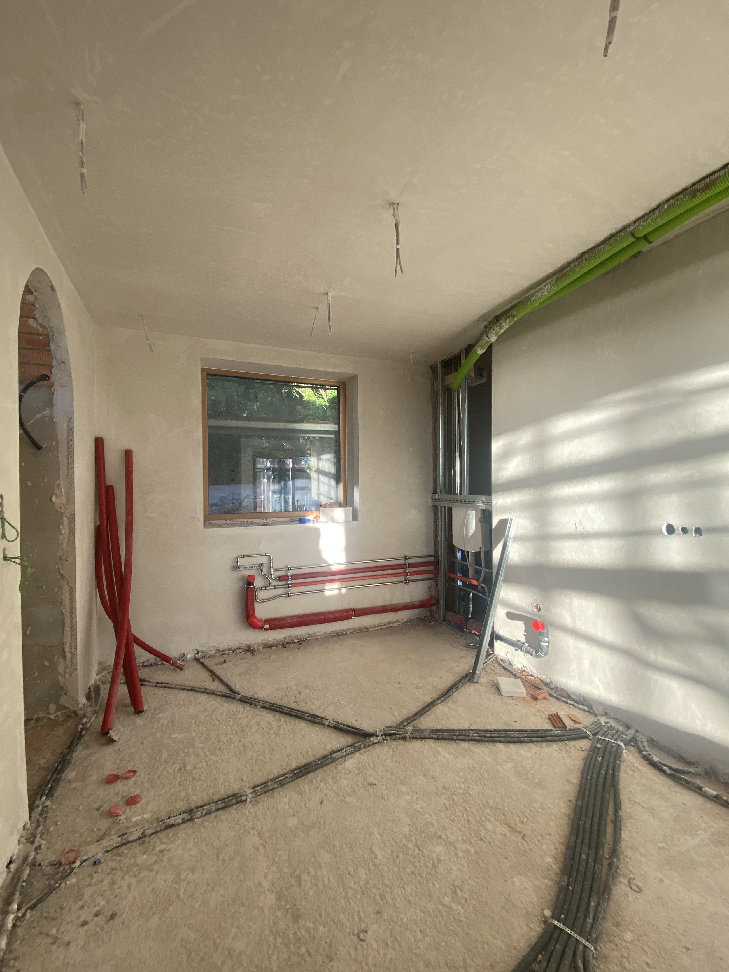 Innenraum eines unvollständigen Hauses im Bau, mit sichtbaren Rohrleitungen, Kabeln und Mauervorbereitungen, keine Möbel, Fenster und unvollständige Wände.