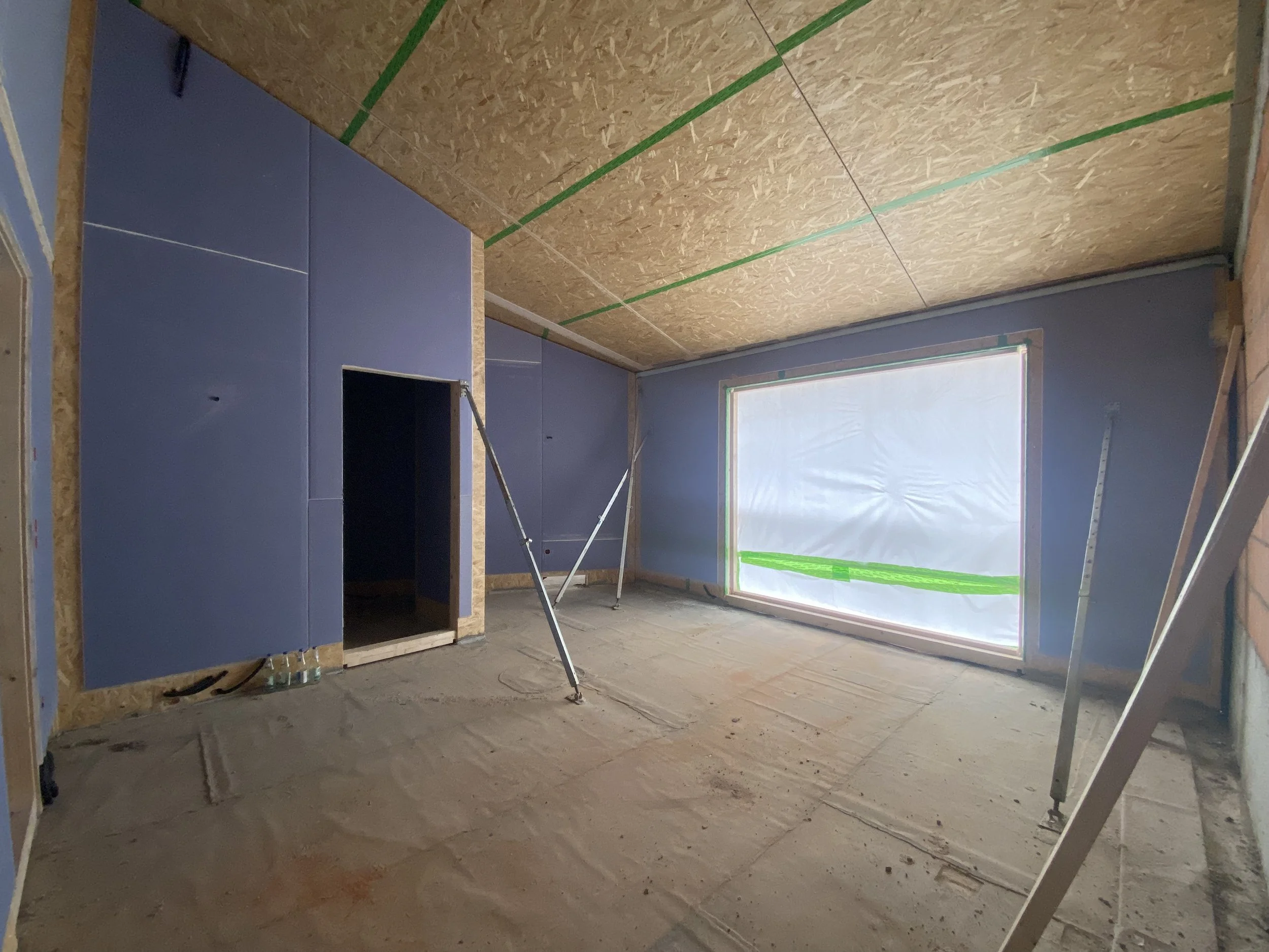 Raumausbau im Inneren eines Hauses mit blau gestrichenen Wandpaneelen, unbefestigtem Boden und einer großen Fensteröffnung.