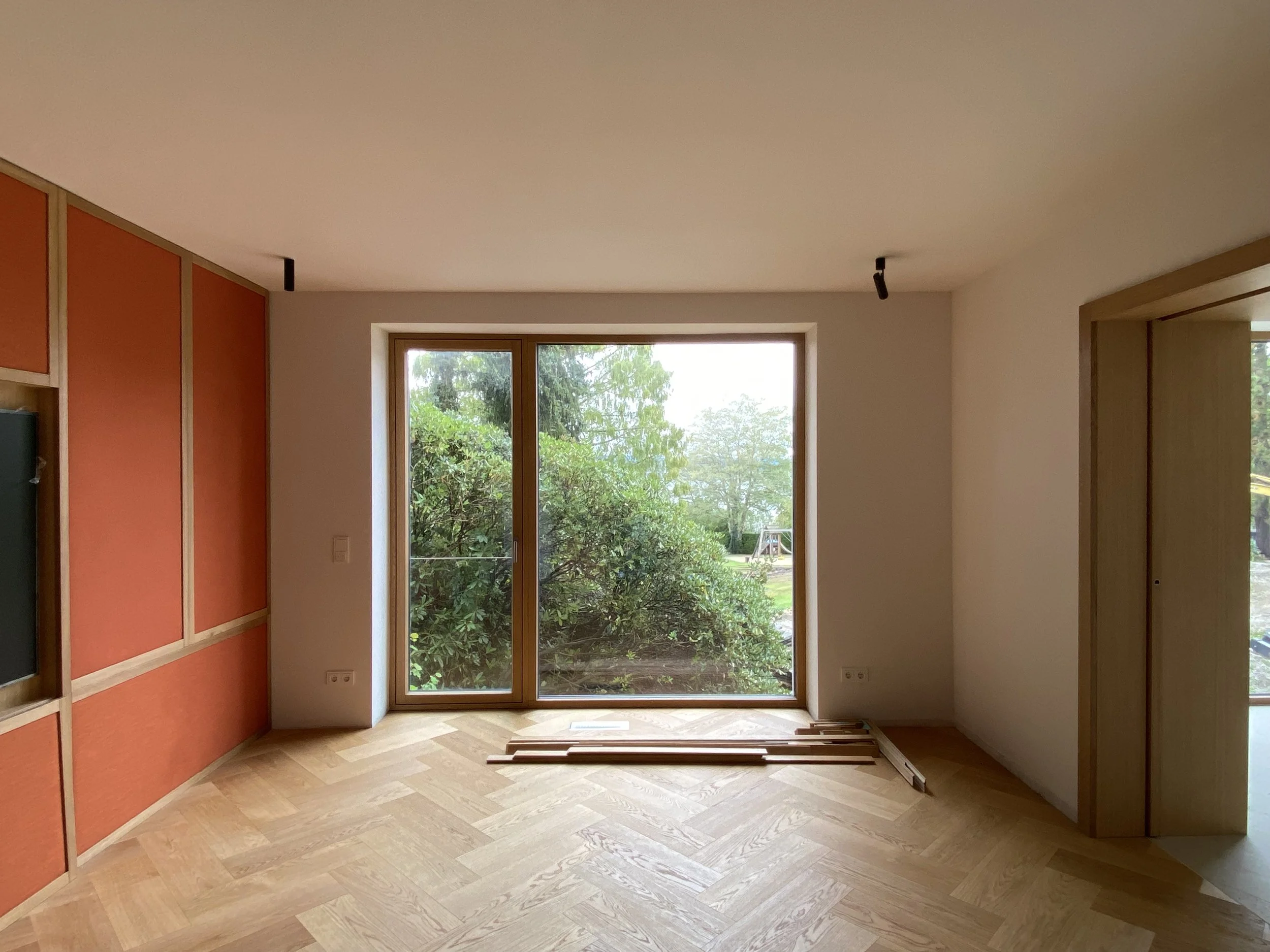 Ein leerer Raum mit großen Fenstern und Holzboden, während der Renovierung, mit Baum und Garten draußen sichtbar.