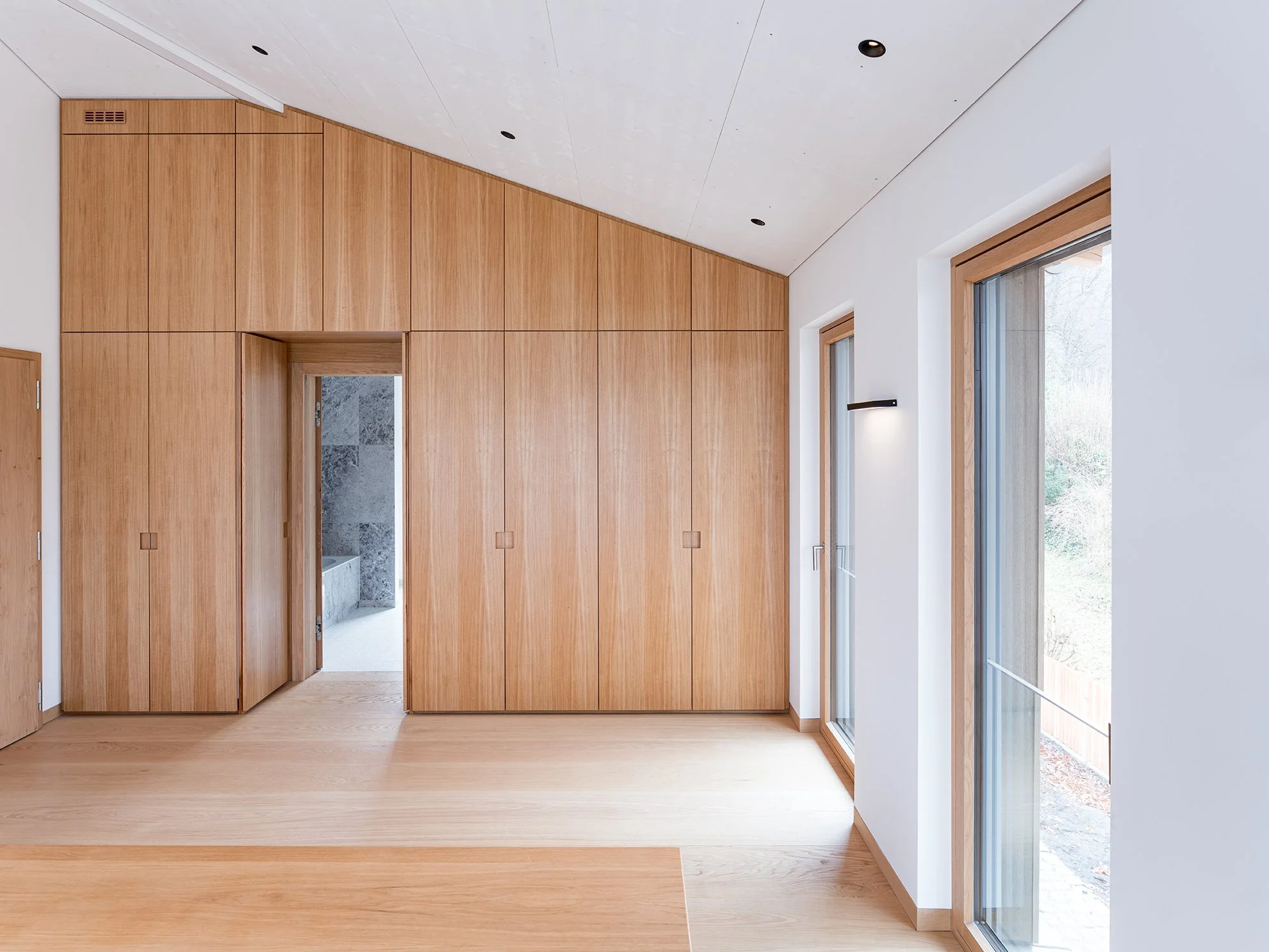 Innenraum mit hellen Wänden, Holztüren und Fußböden, große Fenster mit Holzrahmen, moderner minimalistischer Stil.