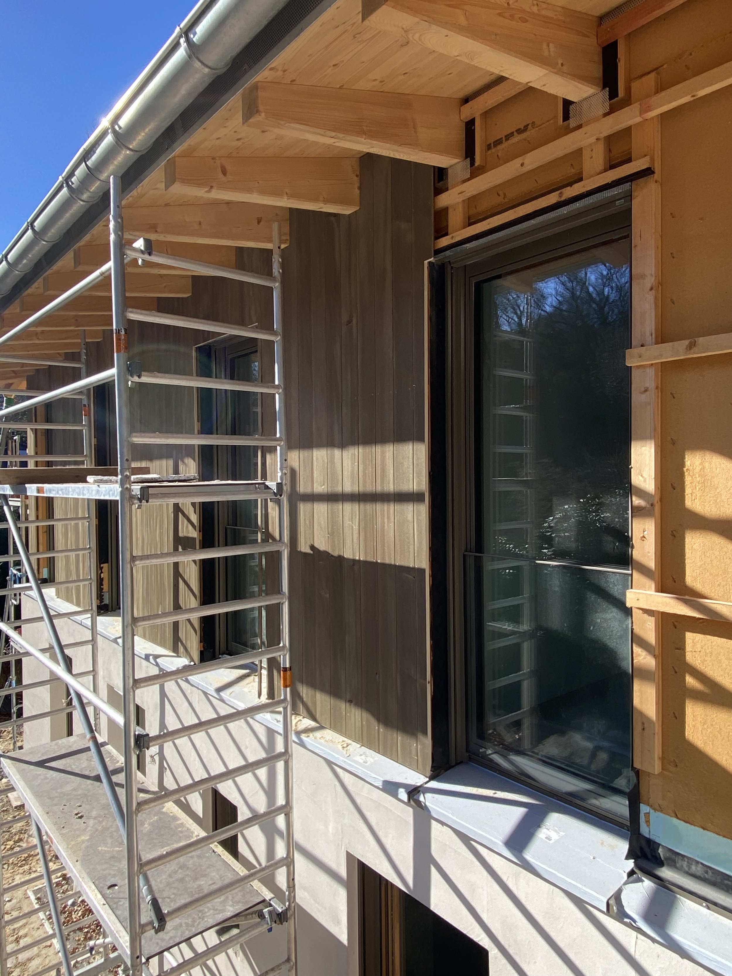 Bauarbeiten an einem mehrstöckigen Gebäude, mit einem Gerüst vor einer Fenstertür und sichtbarem Holzrahmen an der Außenwand.