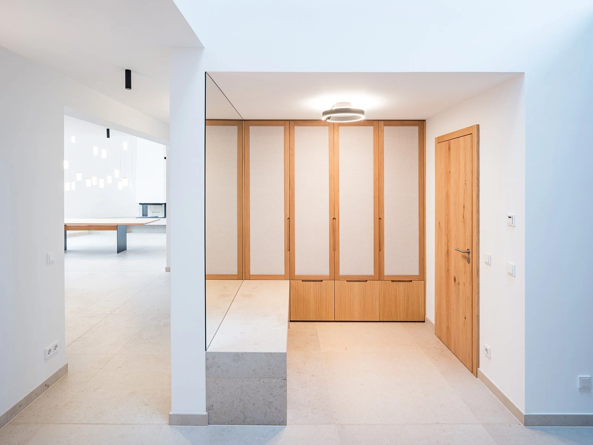 Ein moderner, minimalistischer Eingangsbereich mit Holzschrank, Holztür und weißem Wandbereich.