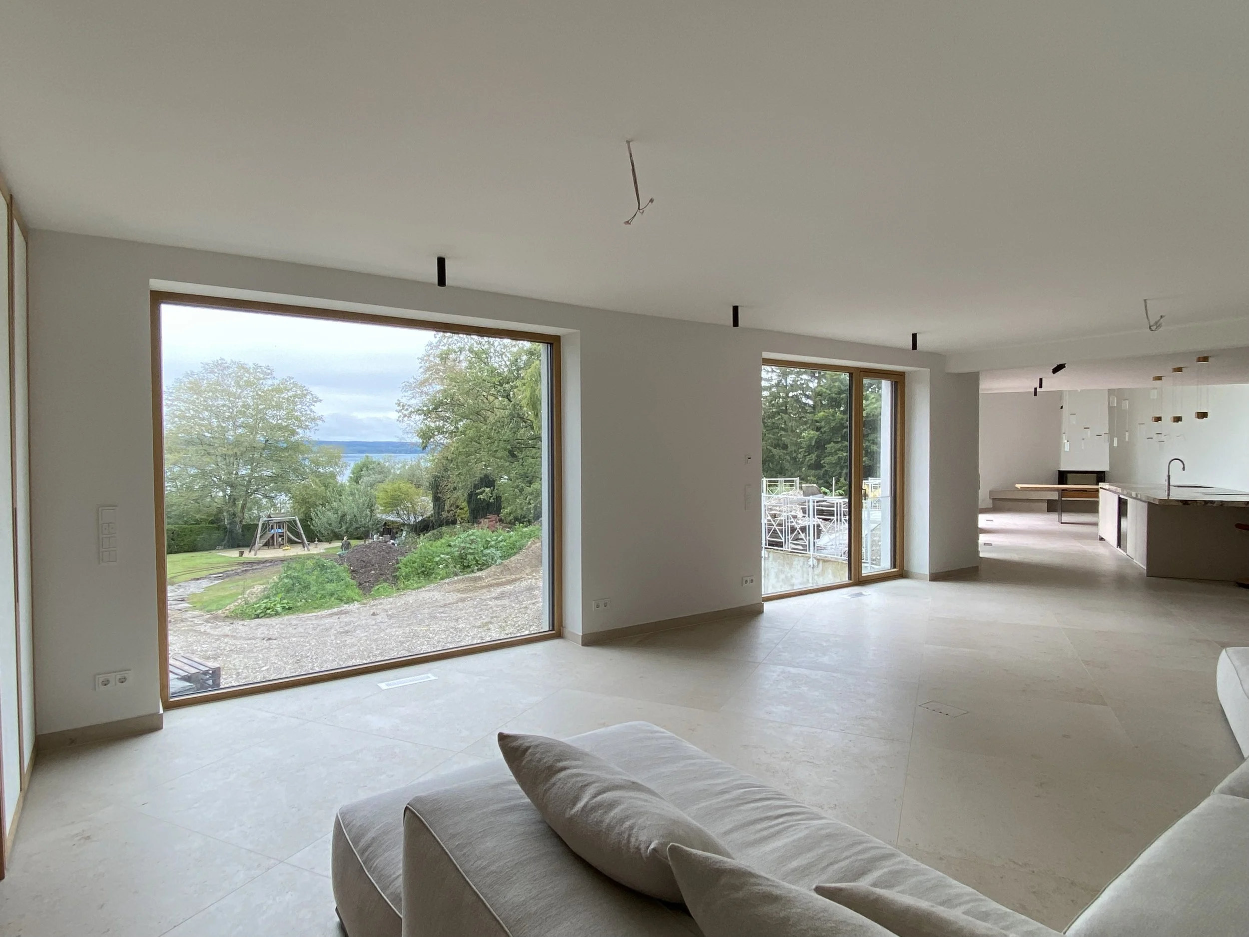 Innenansicht eines unmöblierten, modernen Hauses mit großem Panoramafenster und Blick auf eine grüne Landschaft im Freien.