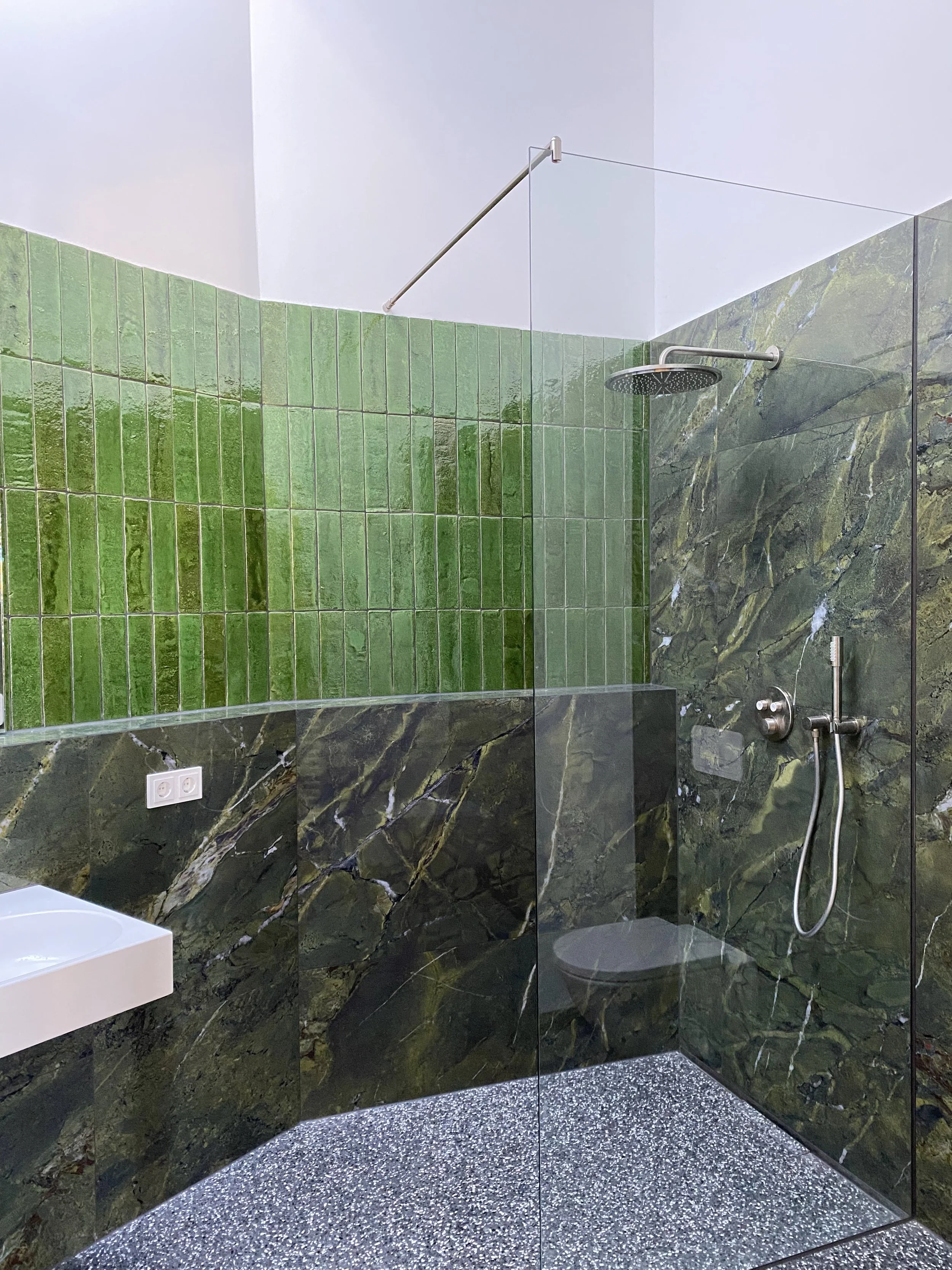 Moderner Duschbereich mit grünen Marmorfliesen an den Wänden, einer Regenbrause und Glasabtrennung.