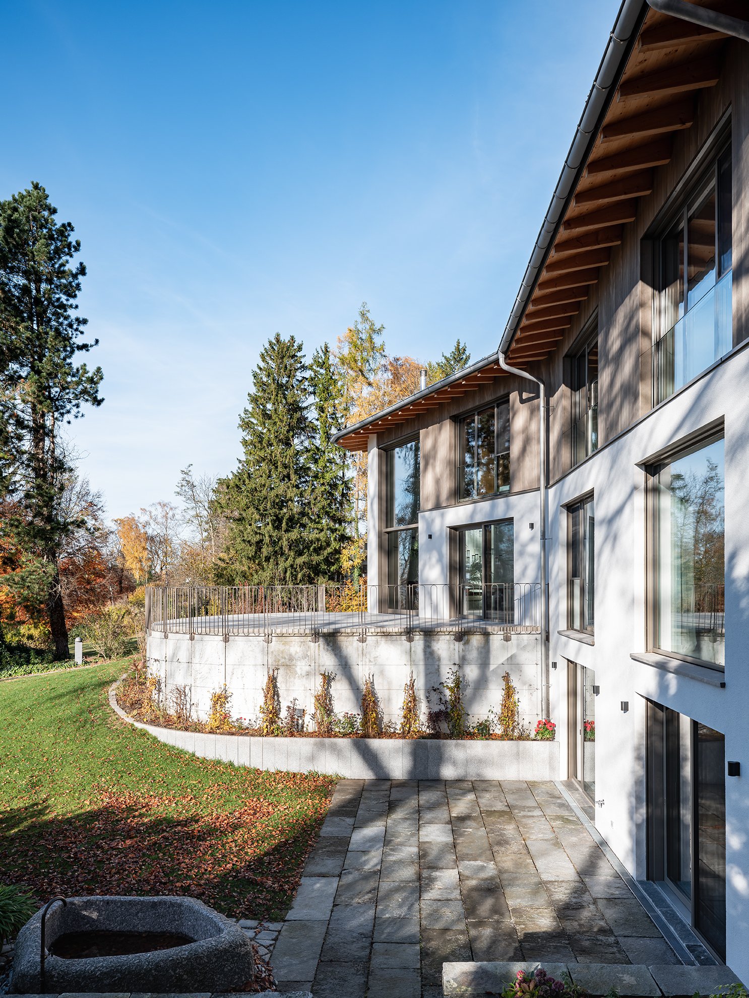 Modernes Mehrfamilienhaus mit Balkon und Garten, umgeben von Bäumen im Herbst, sonniger Tag