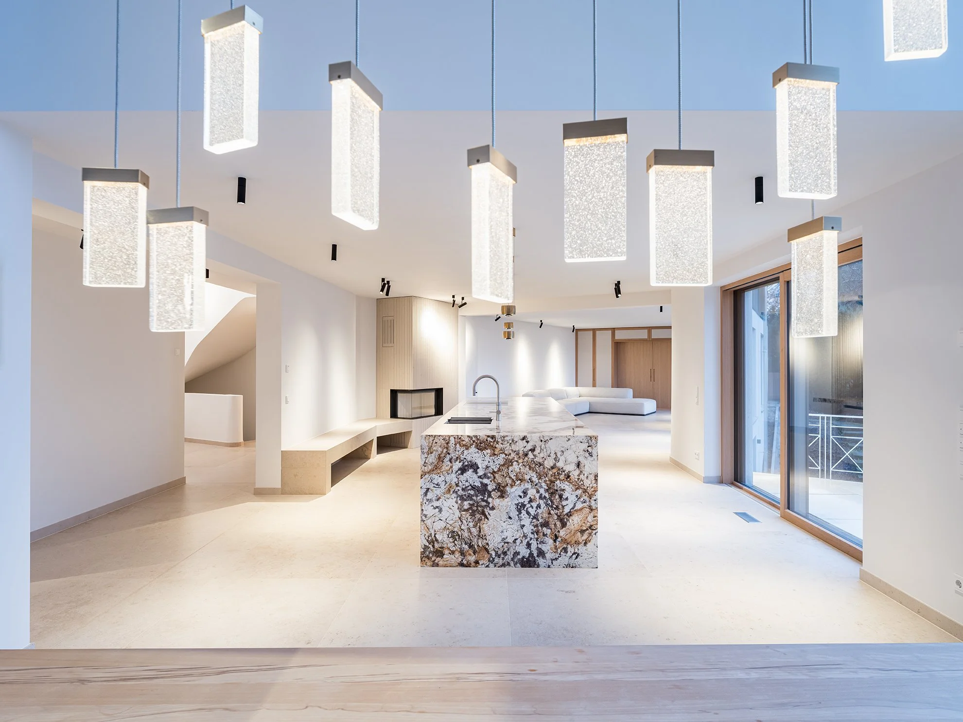 Moderne, offene Küche mit weißem Island aus Marmor, Hängelampen und viel natürlichem Licht durch große Fenster