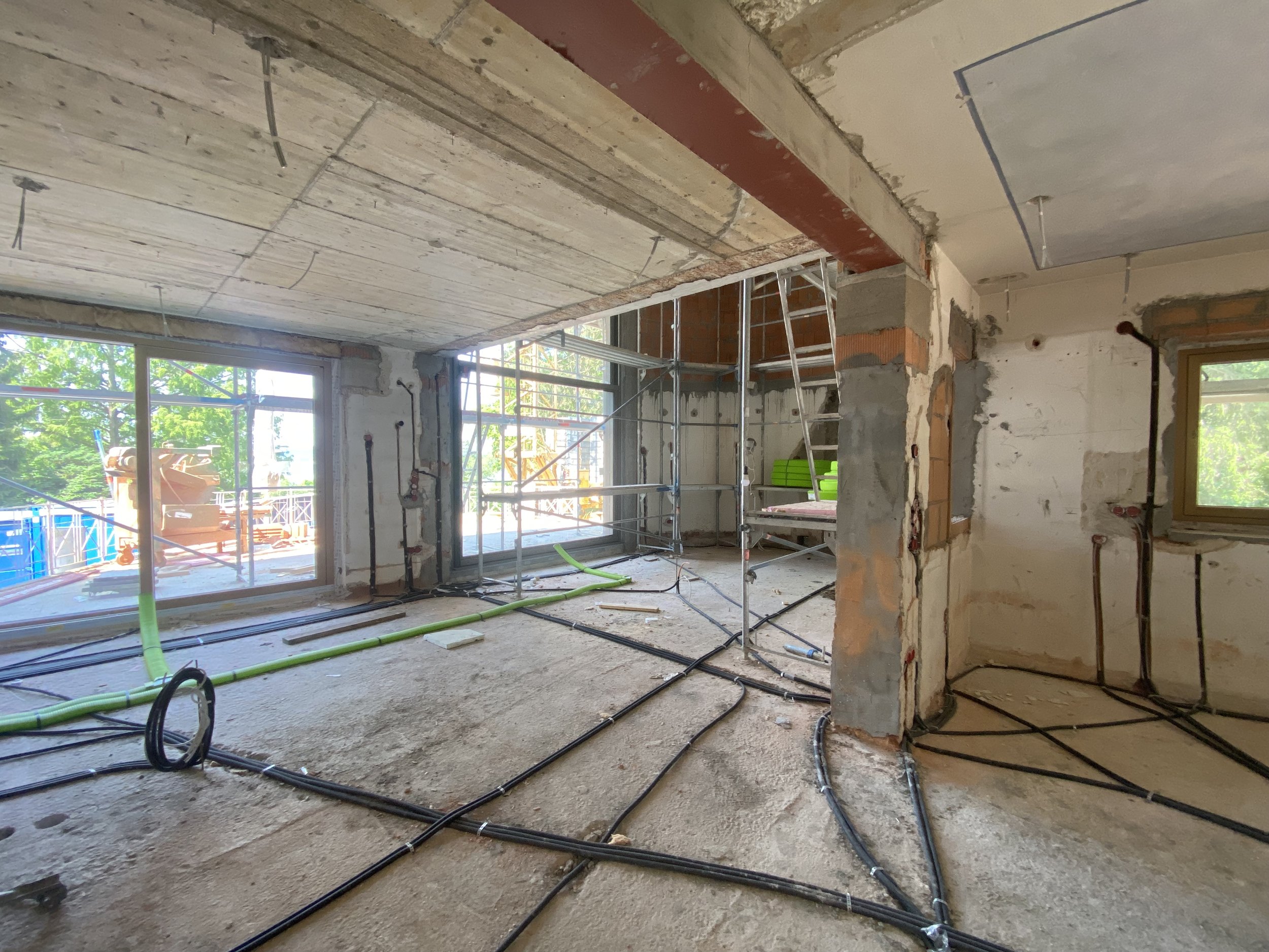 Innenaufnahme eines Bauprojekts, sichtbare Bauarbeiten mit installiertem Elektro- und Sanitärleitungen, Baugerüst im Raum, Fenster zum Außenbereich