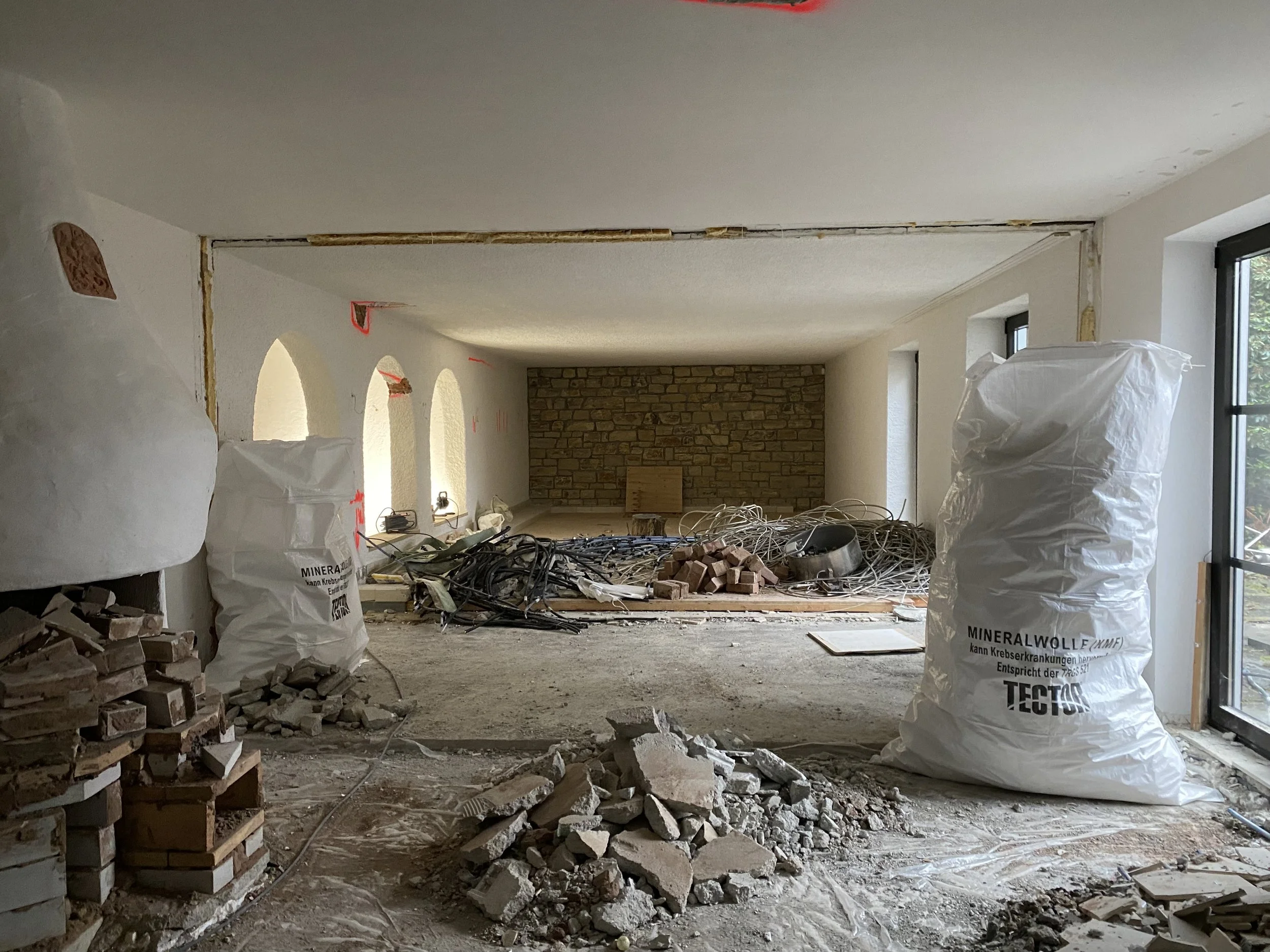 Innenraum einer Baustelle mit zerstörtem Boden, Baumaterialien, Kabeln und Fenstern, es sieht nach Renovierungsarbeiten aus