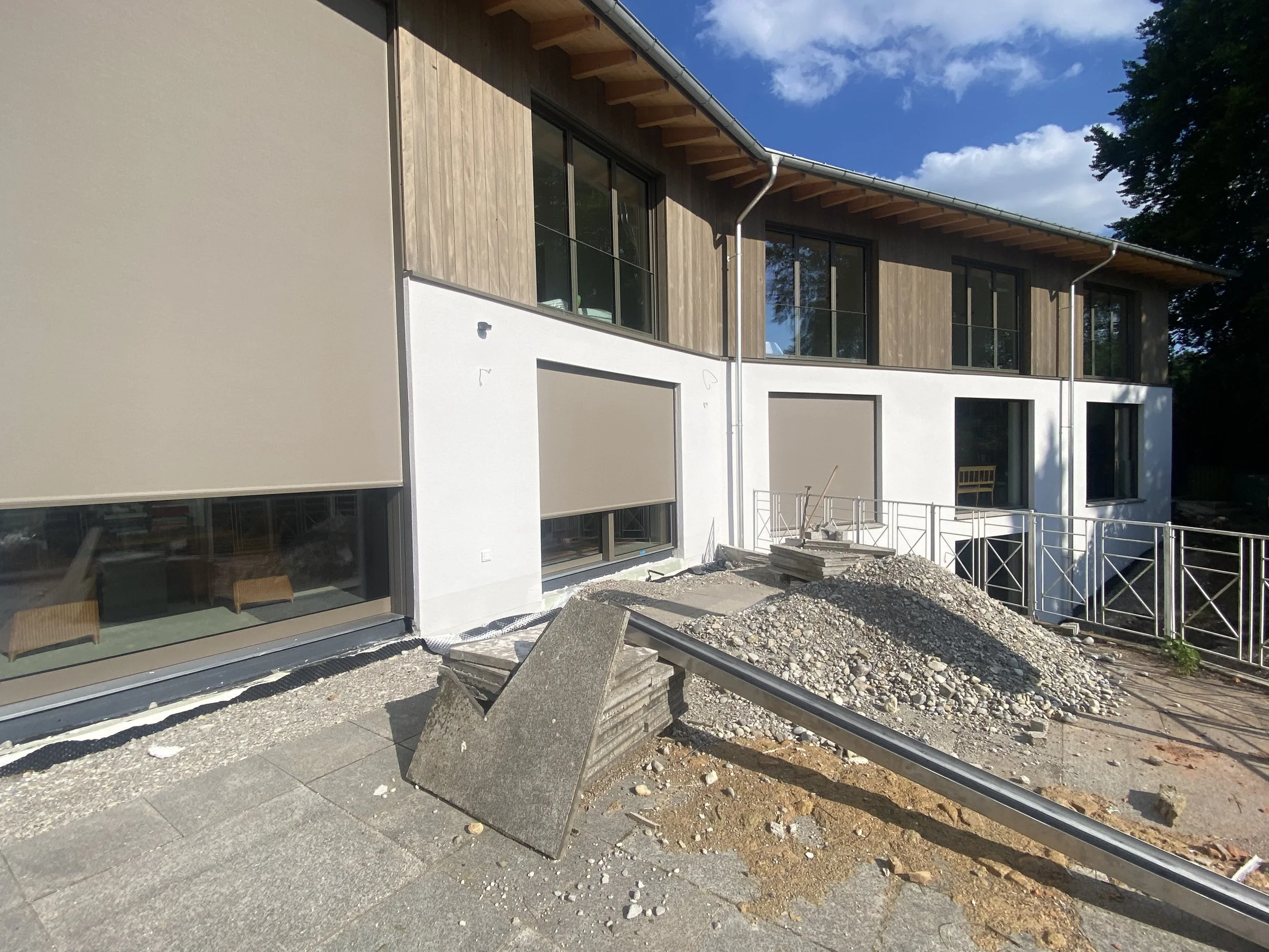 Bauarbeiten an einem mehrstöckigen modernen Haus mit großen Fenstern, Holz- und Weißfassade, und Bauarbeiten im Vordergrund mit Streu und Baumaterialien.