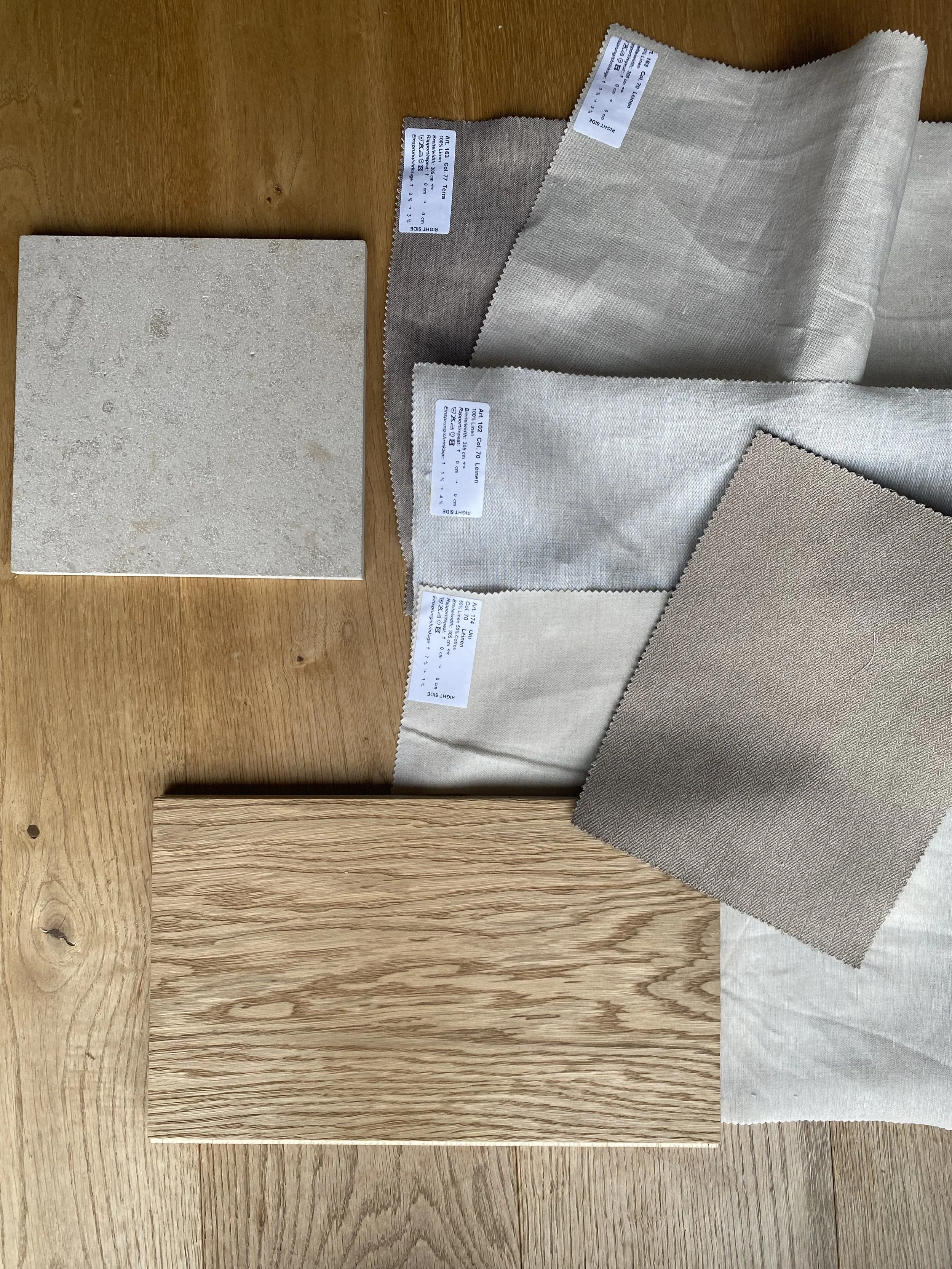 Verschiedene Stoffproben, eine Fliese und Holzplatte auf einem Holztablett, vermutlich für Inneneinrichtung.