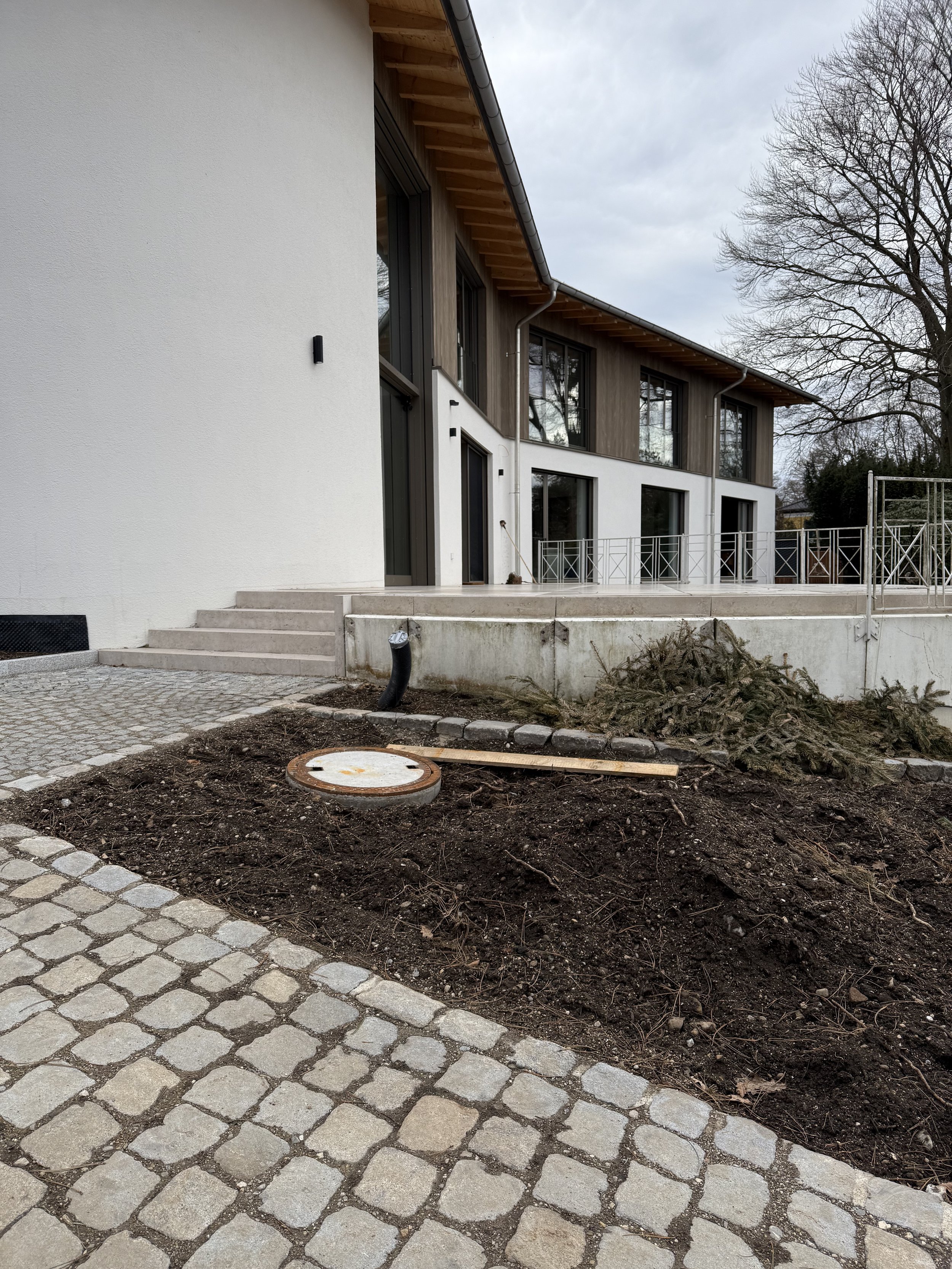 Modernes Haus im Bau mit einer Gartenfläche und Pflastersteinen, einige Bauarbeiten und Erde im Vordergrund.