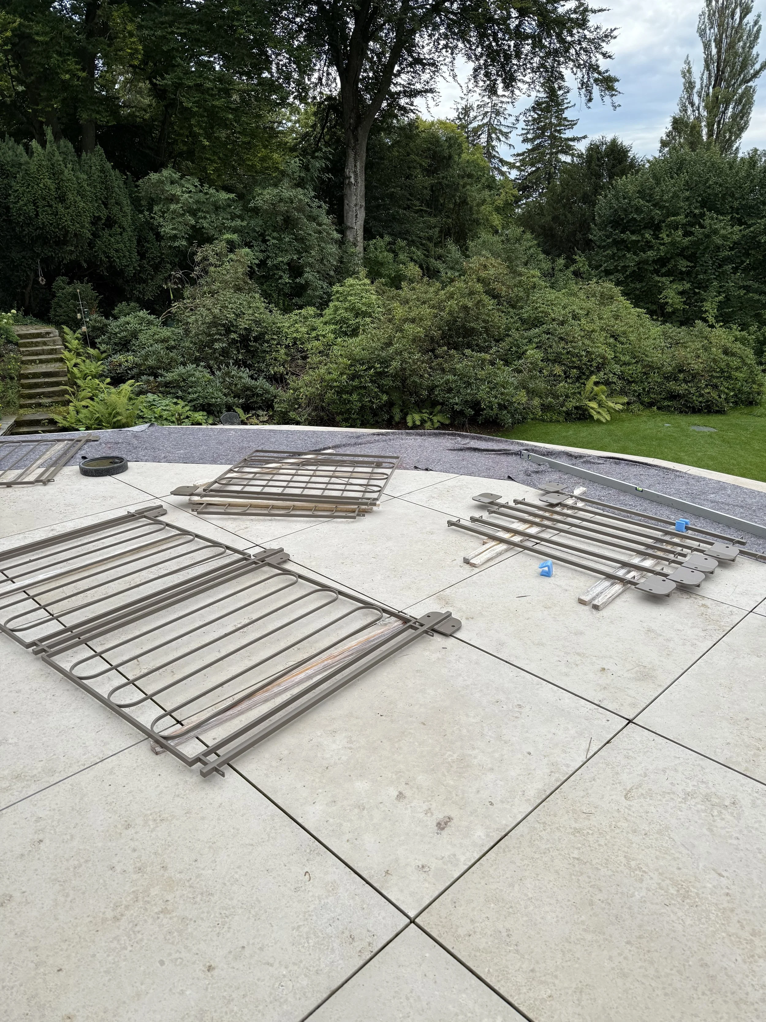 Abgebaute Gartengitter auf weißem Terrassenboden mit Garten und Bäumen im Hintergrund.