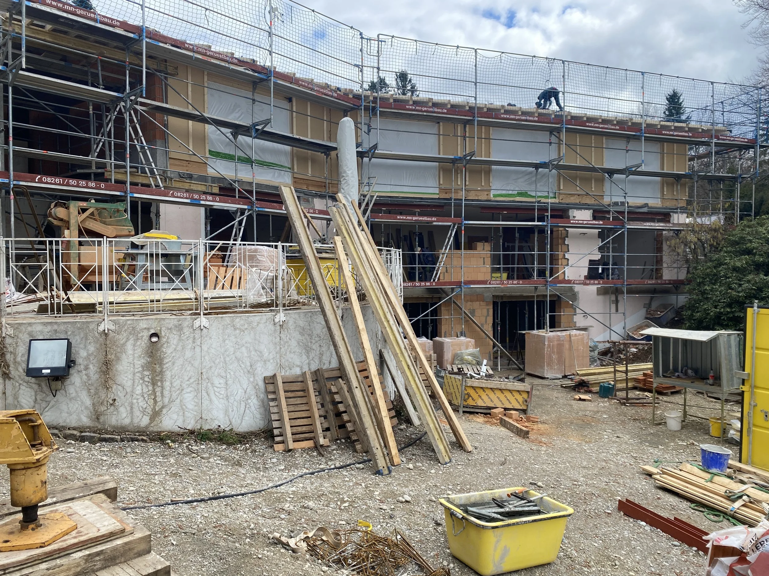 Baustelle mit Baugerüsten und Bauarbeiten an einem mehrstöckigen Gebäude, Holzbohlen, Baumaterialien und Werkzeuge im Vordergrund