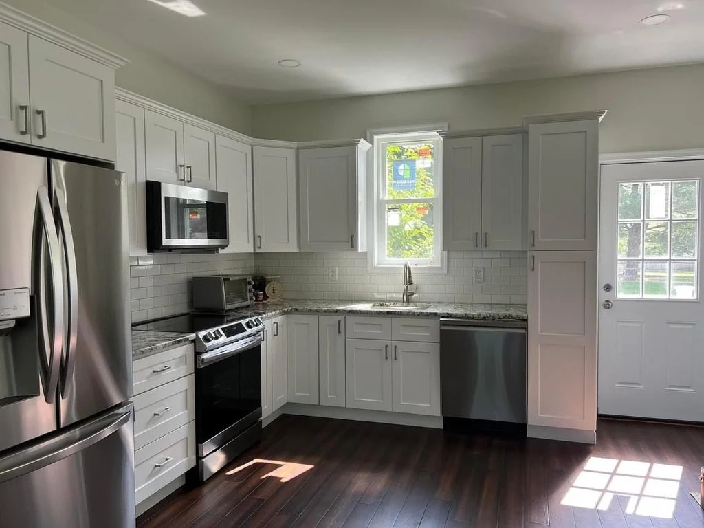 Modern kitchen with white cabinets, stainless steel appliances, granite countertops, a subway tile backsplash, a small window above the sink, and a glass-paneled door.
