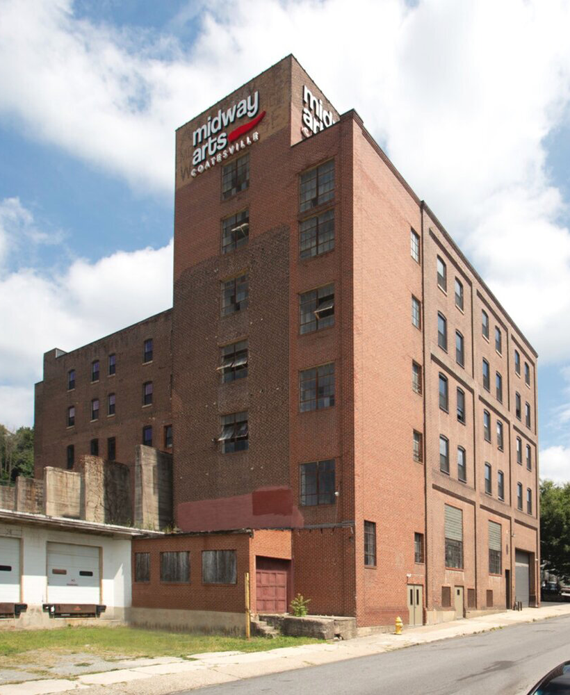 A tall brick building with three signs on top, one reading 'midway arts Coatesville'.