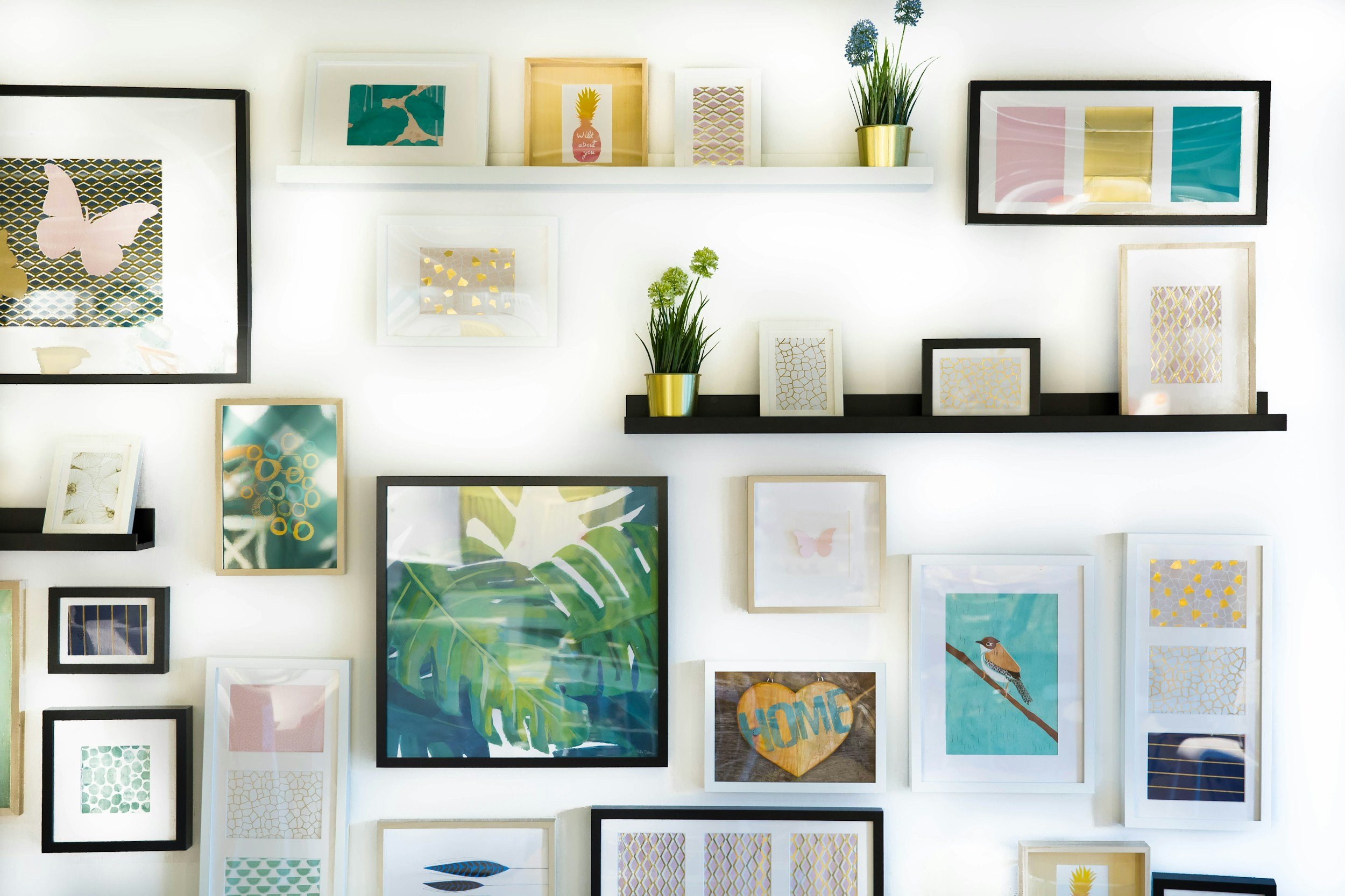Decorative wall with framed pictures, artwork, and potted plants