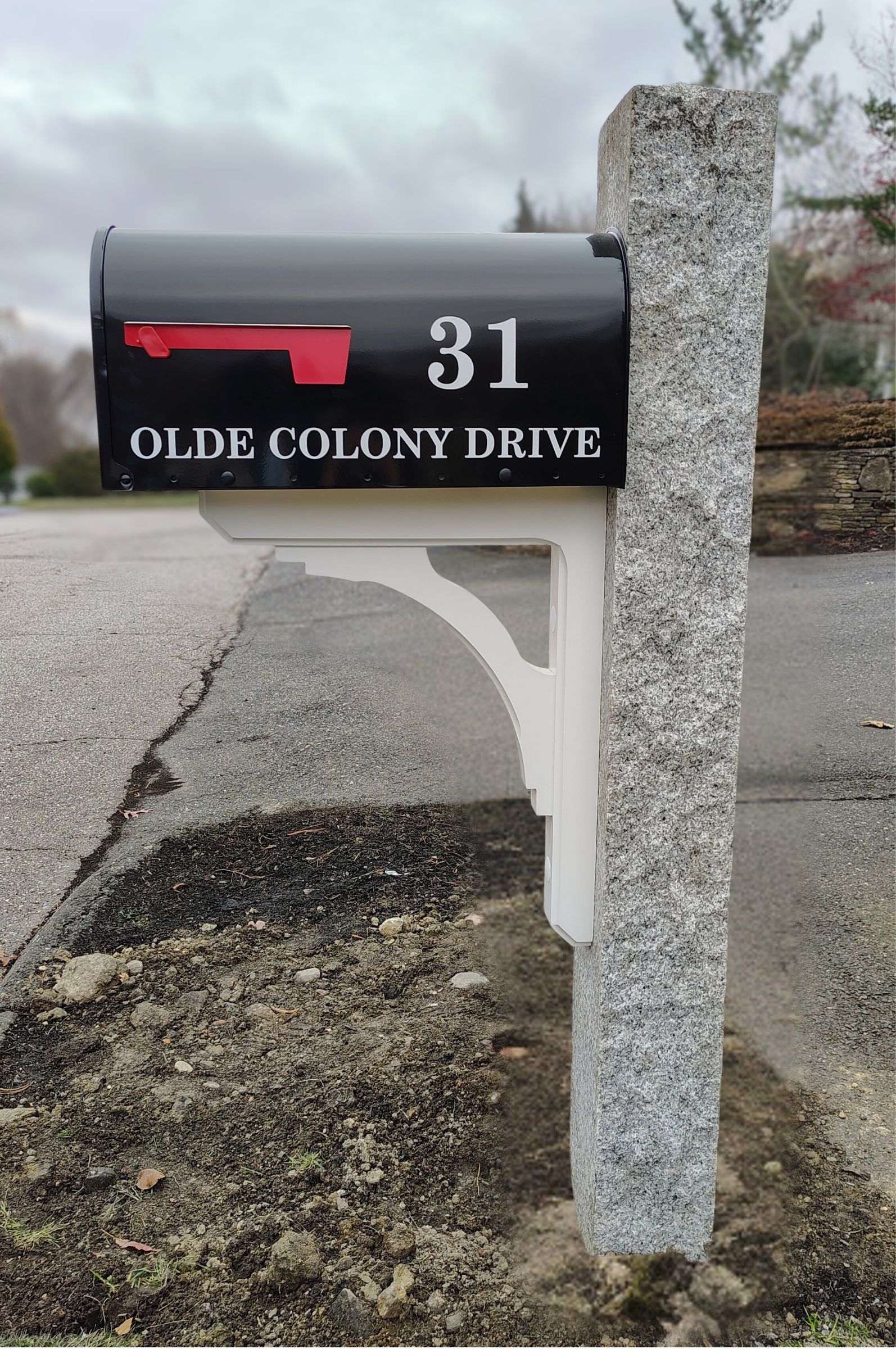 Black mailbox with red flag, labeled 31, mounted on a white decorative post back with a stone pillar, on Olde Colony Drive, with a suburban street in the background.