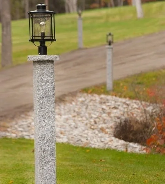 A decorative outdoor lamp post on a stone pedestal along a walking path in a grassy area.