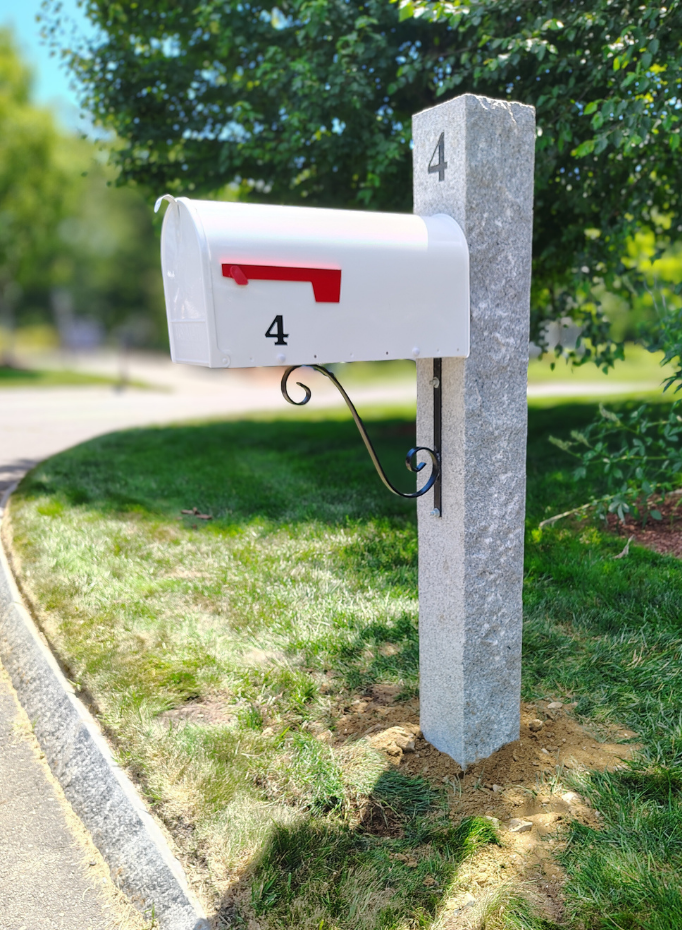7x7 granite mailbox post featuring an iron scroll bracket, a white gibraltar mailbox,  the number 4 engraved, and a black address decal
