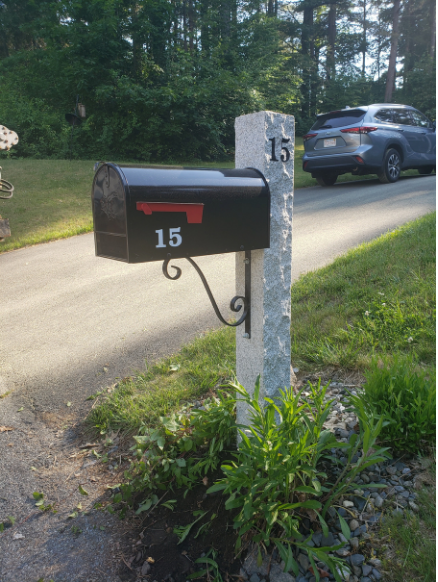 Black mailbox with the number 15 on a stone post beside a driveway, with a parked silver SUV in the background.