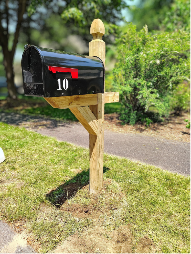 wooden mailbox post with a black mailbox installed next to a driveway