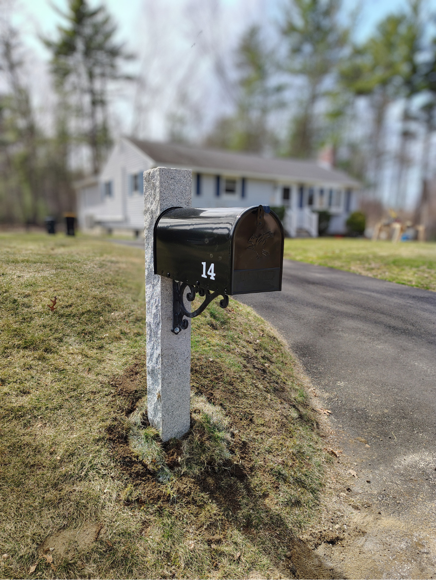 Black mailbox with the number 14 on a concrete post in front of a house with a driveway and lawn.