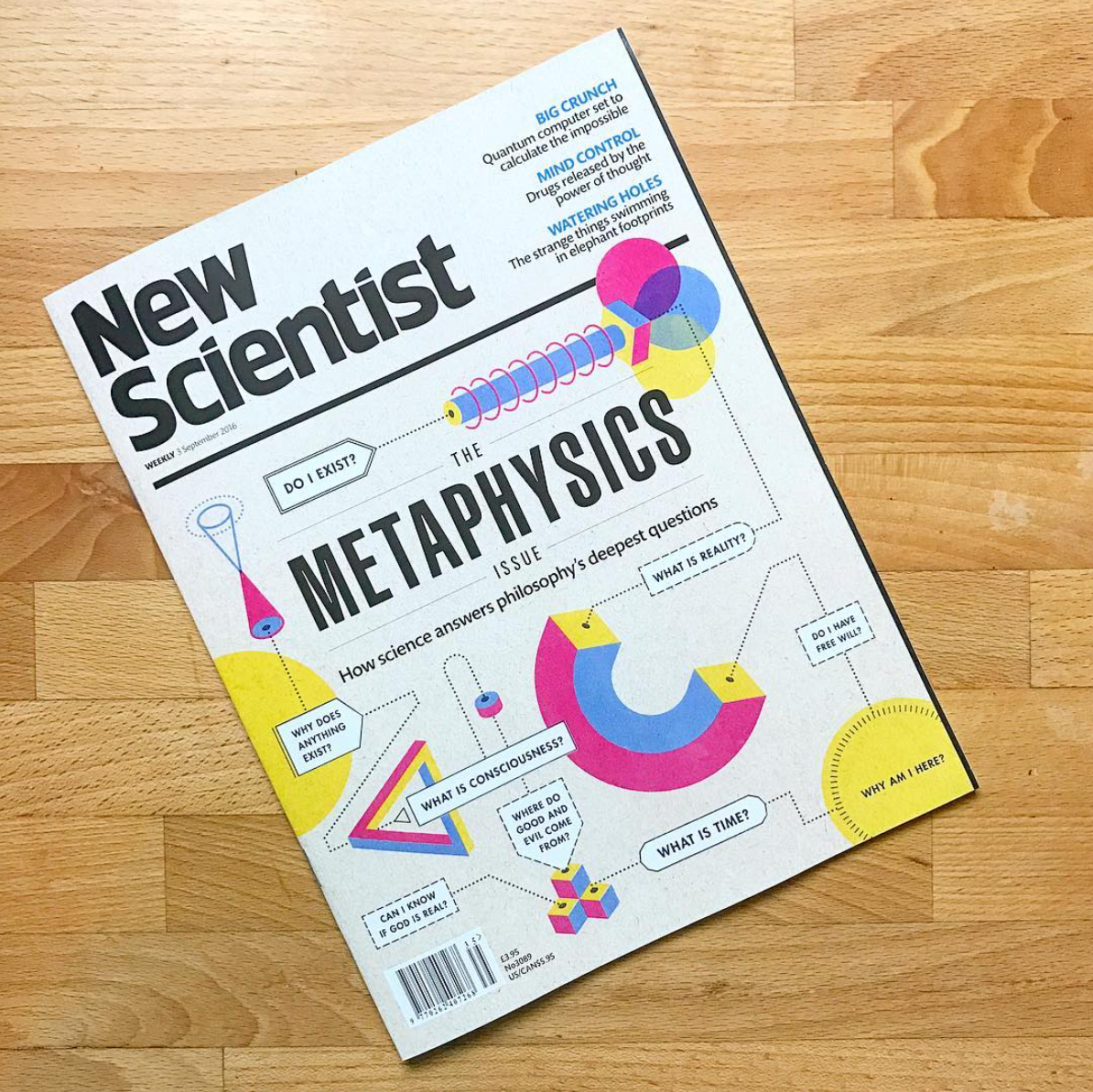 Magazine titled 'New Scientist' featuring an issue on the metaphysics of science with colorful illustrations of geometric shapes and scientific questions on a wooden surface.