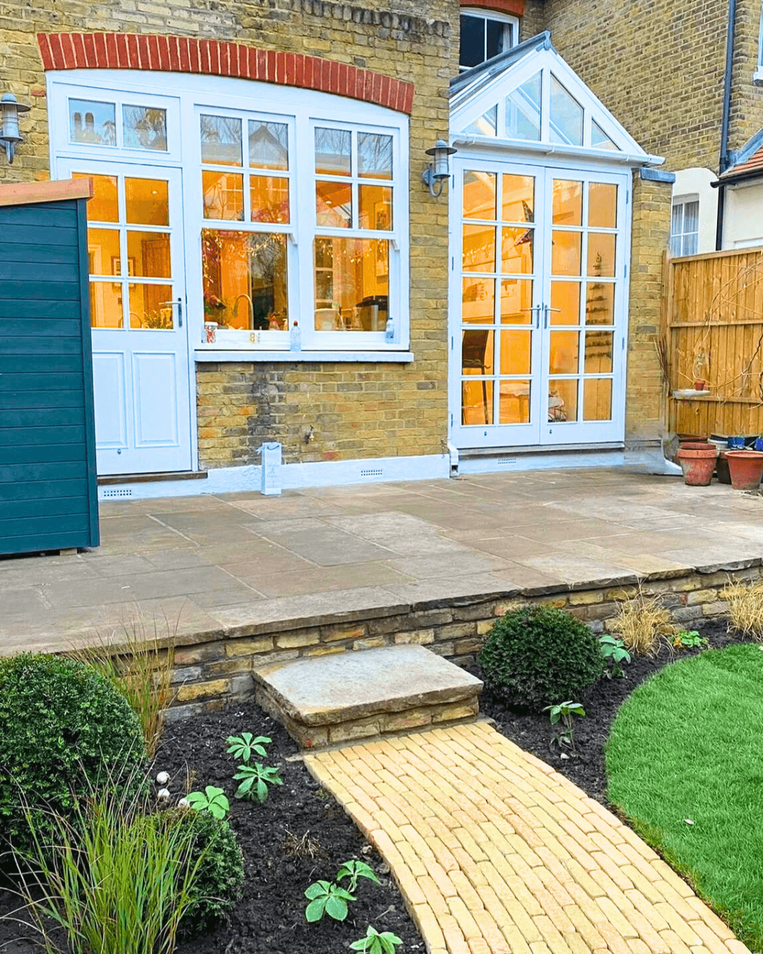 Landscaped garden with stone patio, brick pathway and planting beds outside a Victorian home in Richmond, London.