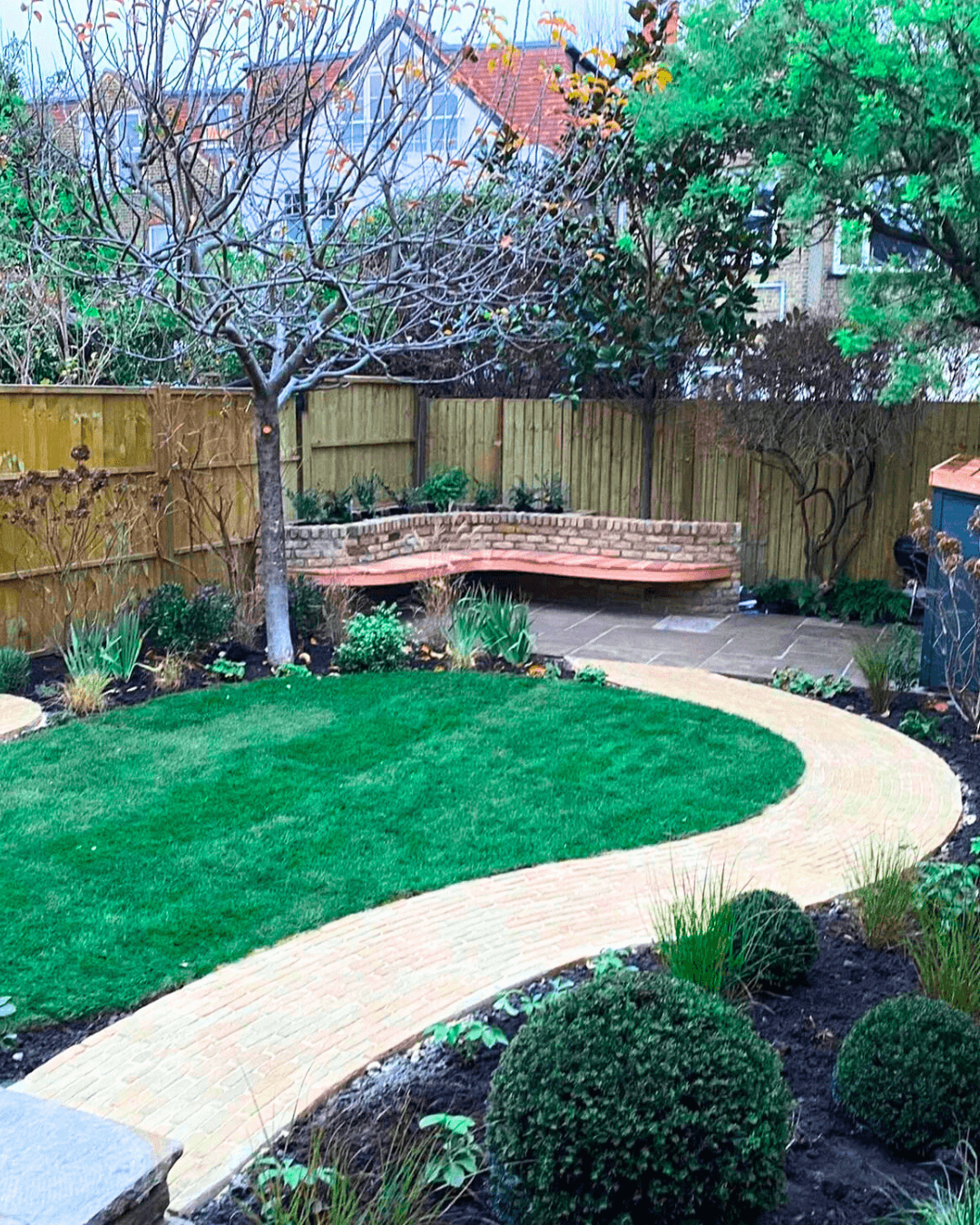 Professional garden landscaping project in Richmond London with curved brick pathway, lawn and raised seating area.