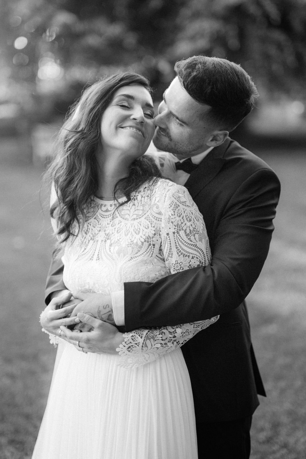 Ein glückliches Paar in formeller Kleidung, das sich umarmt, im Freien bei Sonnenuntergang, Schwarz-Weiß-Foto. Die Hochzeit findet im Schloss Grünewald bei Düsseldorf, Nähe Köln statt. 