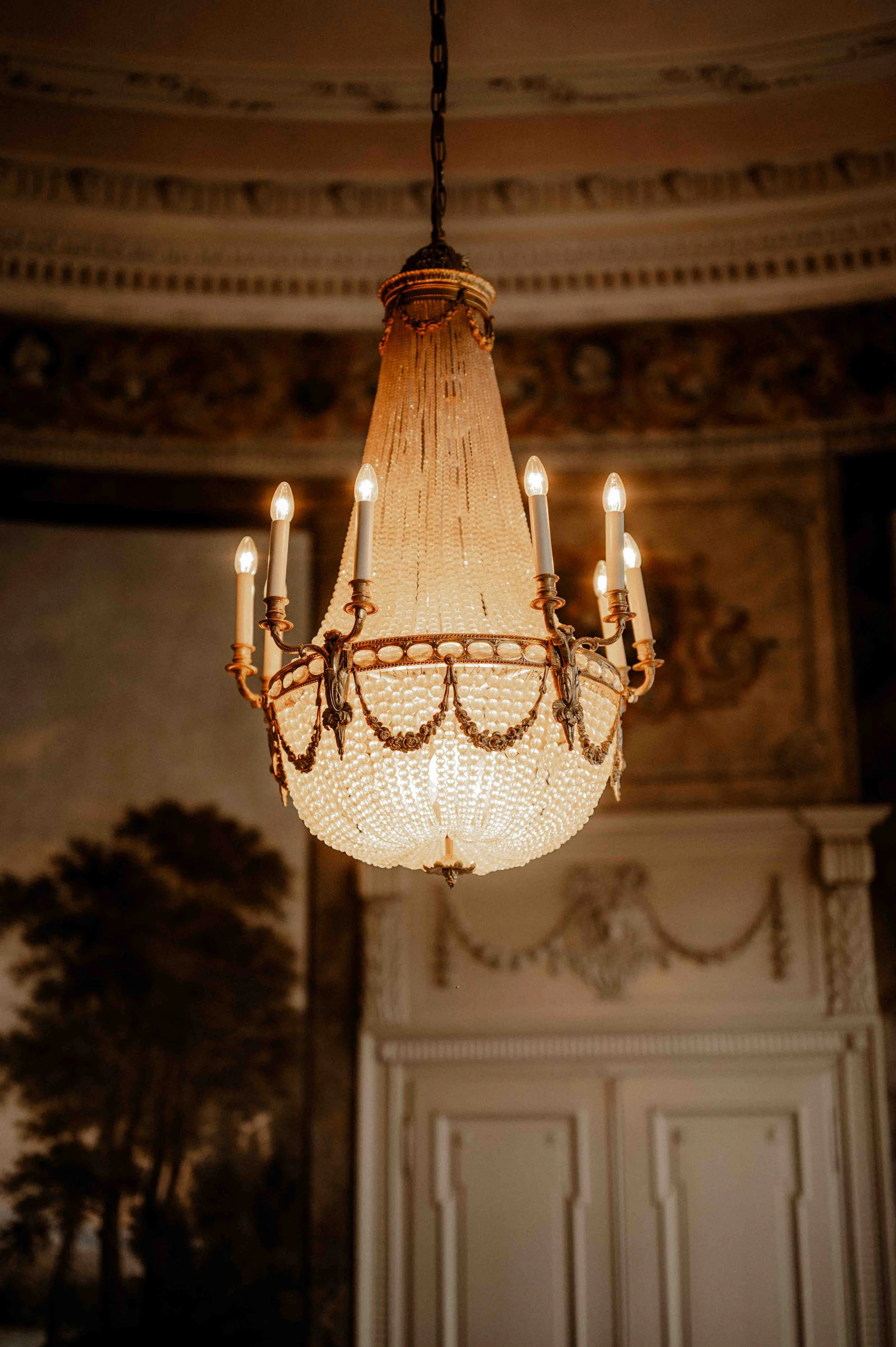 Ein prunkvoller Kristall-Kronleuchter mit Kerzen in einem eleganten, historischen Raum mit aufwendiger Deckenverzierung. Die Hochzeit findet in Düsseldorf, Nähe Köln statt. 