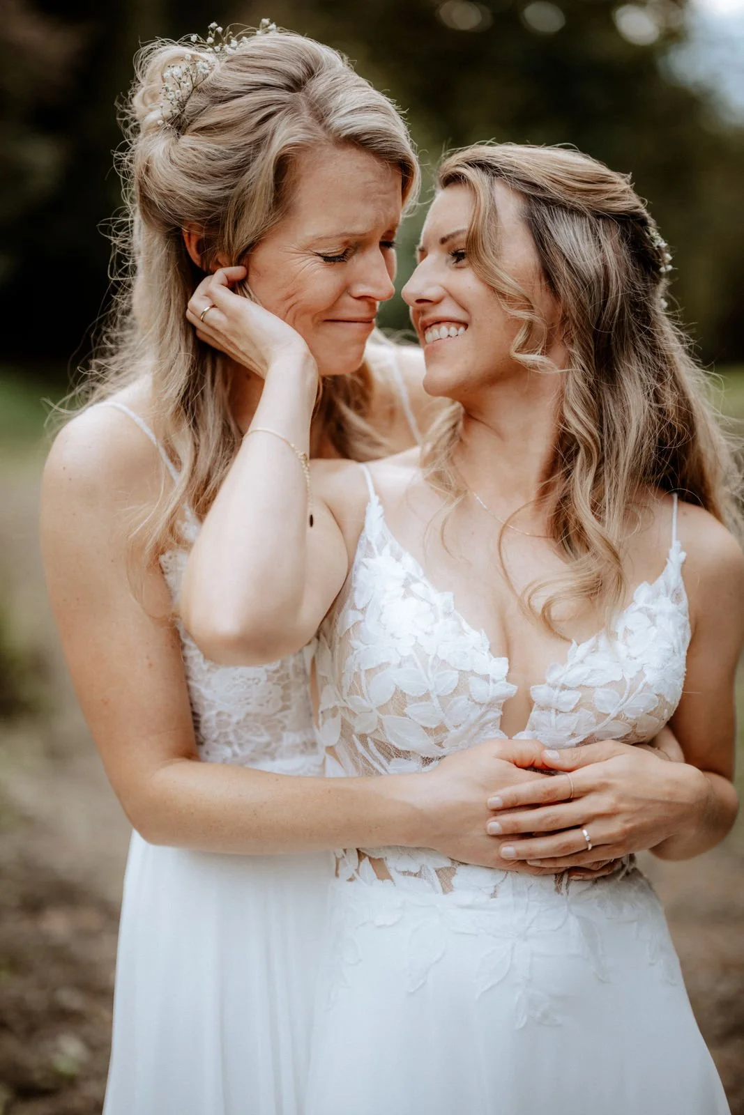 Zwei Frauen in weißen Brautkleidern, die sich liebevoll umarmen und eine emotionale Umarmung zeigen. Die Hochzeit findet in Leichlingen im Sinneswald bei Düsseldorf, Nähe Köln statt. 
