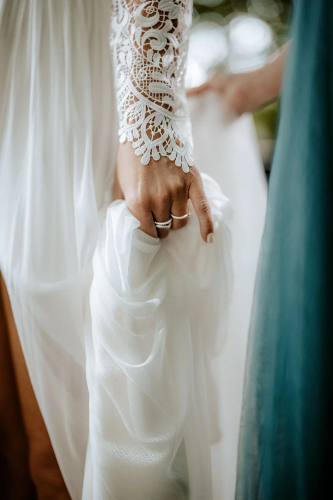 Eine Hand in einem weißen Brautkleid mit spitzenärmeligen Ausschnitt, die eine andere Person hält. Die Hochzeit findet in Düsseldorf, Nähe Köln statt. 