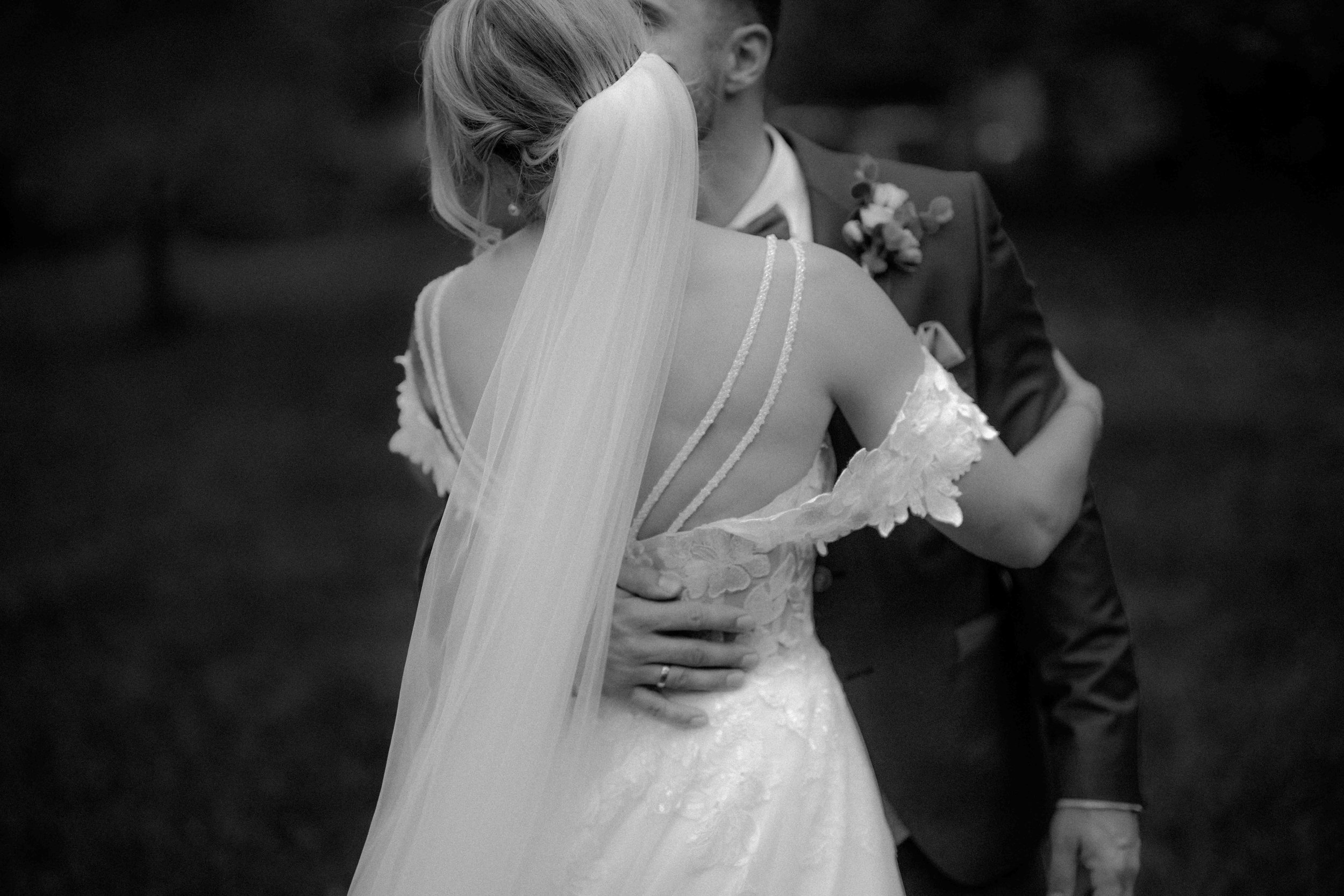 Ein Paar bei einer Hochzeit, das sich küsst. Das Brautkleid ist zart und hat Spitzen-Details, der Bräutigam trägt einen Anzug mit Krawatte. Das Bild ist in Schwarz-Weiß gehalten. Die Hochzeit findet in Düsseldorf, Nähe Köln statt. 