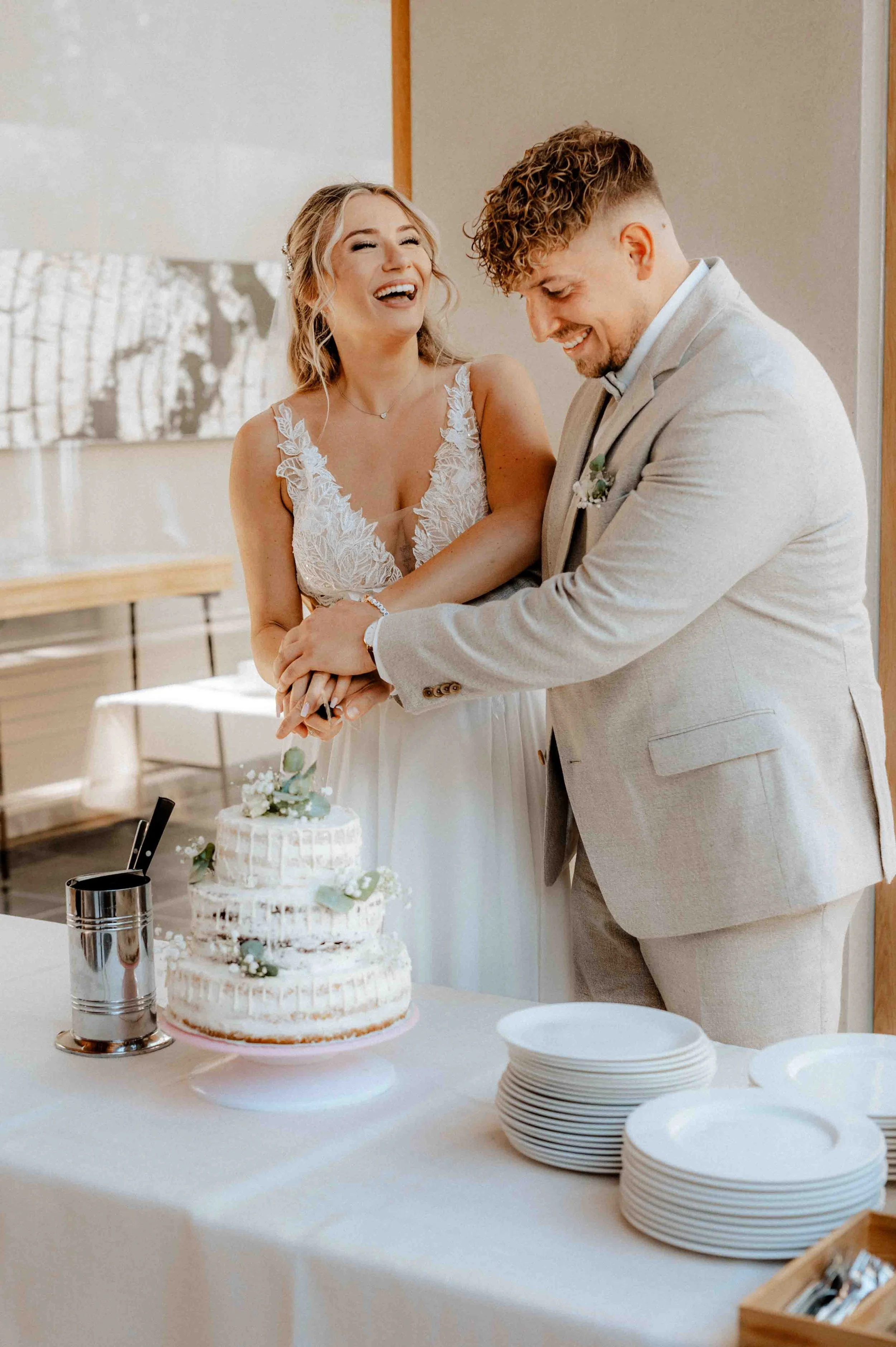 Ein Brautpaar schneidet eine Hochzeitstorte gemeinsam an, lachend und glücklich, bei einer Hochzeitsfeier. Die Hochzeit findet in Düsseldorf, Nähe Köln statt. 