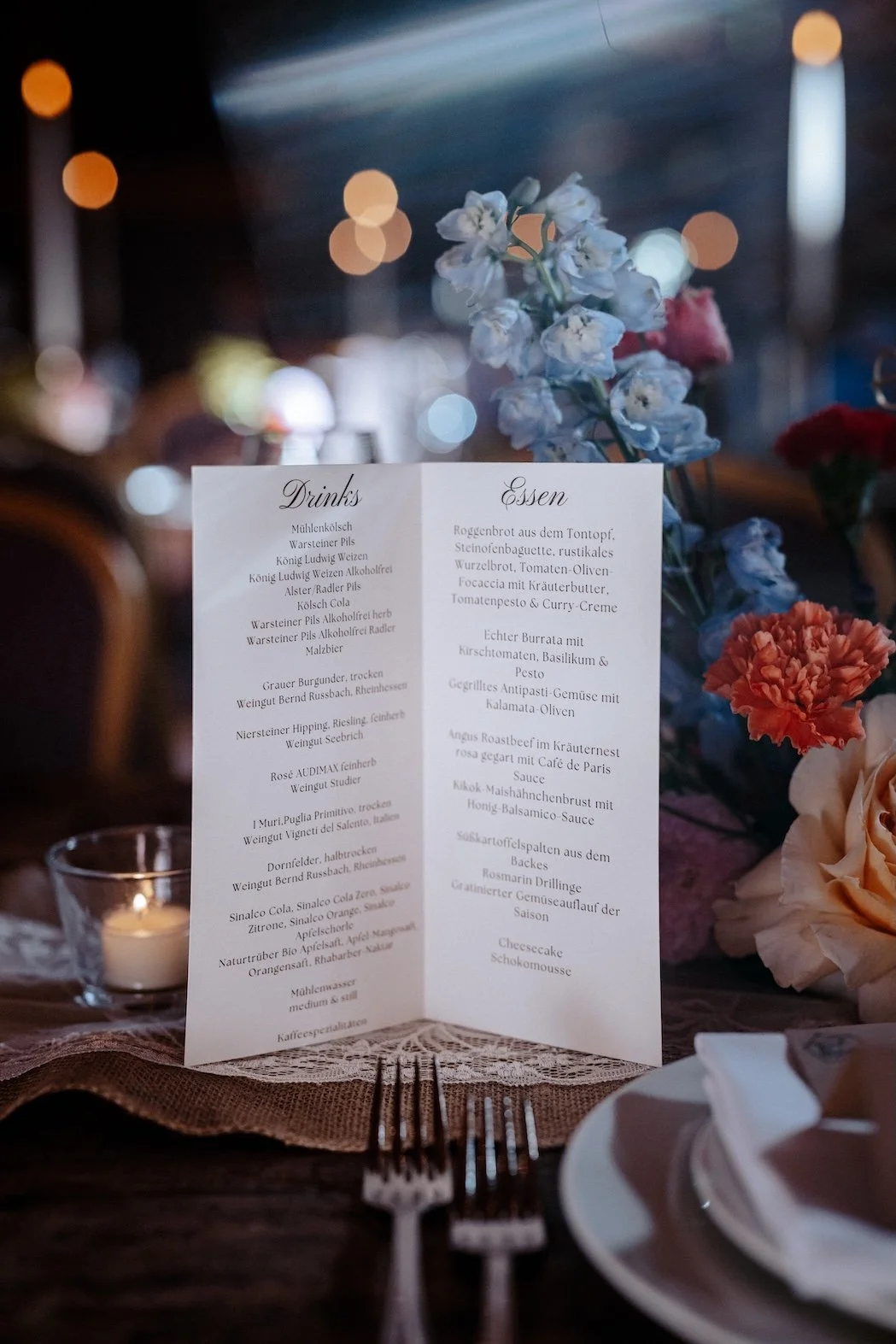 Menükarte auf einem festlich gedeckten Tisch mit Blumen, Besteck und einer Kerze im Glas. Die Hochzeit findet in Düsseldorf, Schloss Benrath statt. 