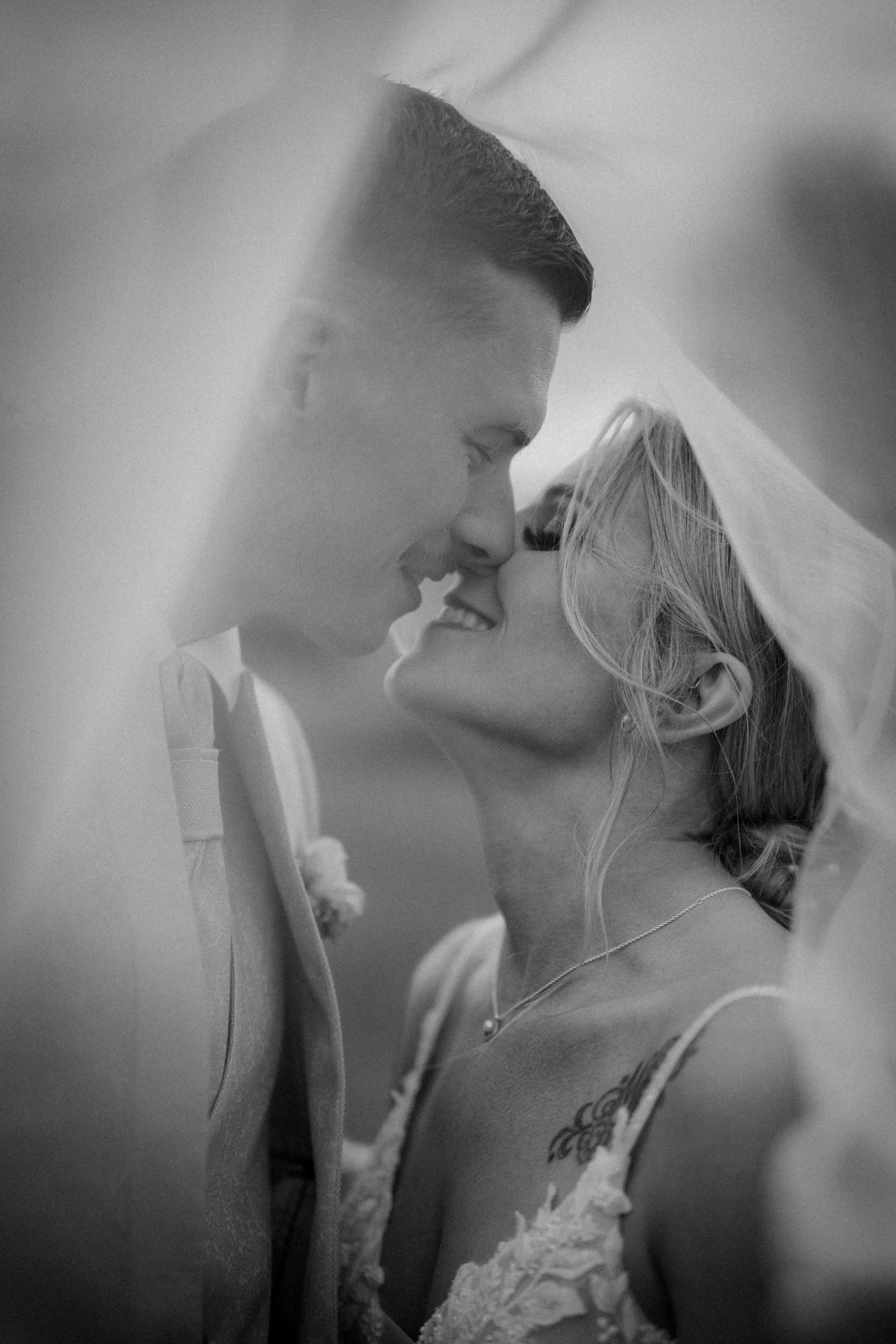 Braut und Bräutigam beim Hochzeitsshooting, stehen sich nahe, lachen und berühren mit ihrer Nasen, Blick aufeinander, in Schwarz-Weiß. Die Hochzeit findet in Düsseldorf, Nähe Köln statt. 