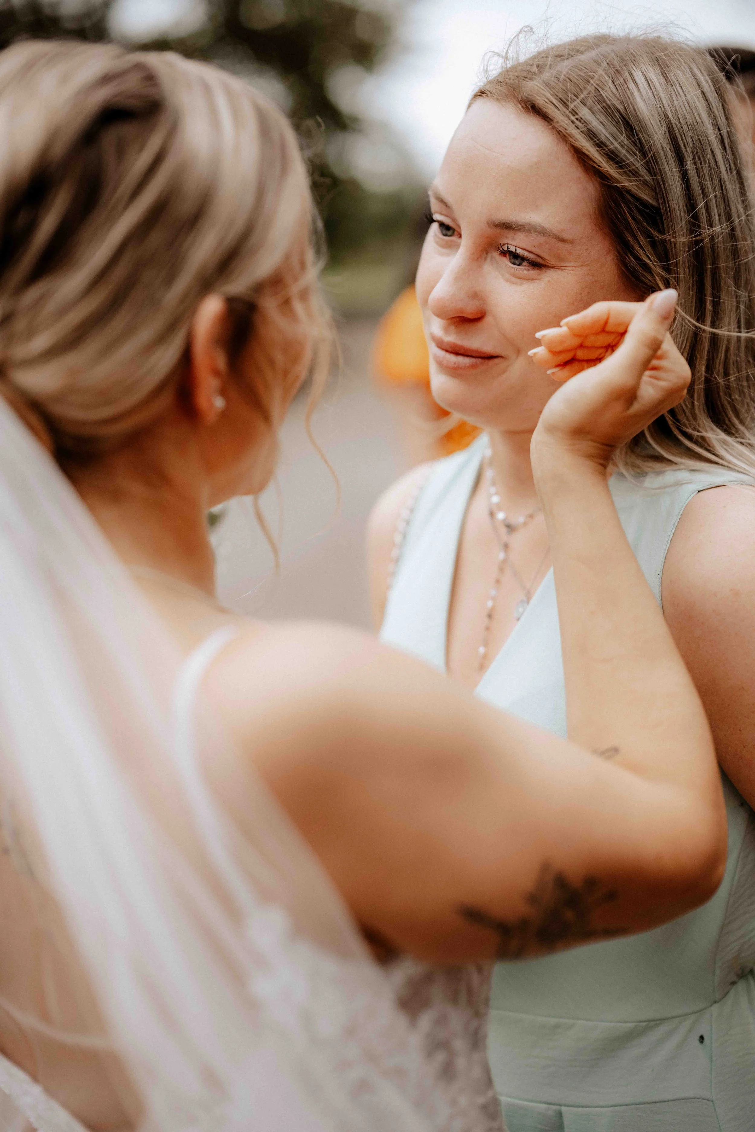 Zwei Frauen bei einem emotionalen Moment, vermutlich bei einer Hochzeit, wobei eine Frau die andere sanft berührt und emotional berührt wirkt. Die Hochzeit findet in Düsseldorf, Nähe Köln statt. 