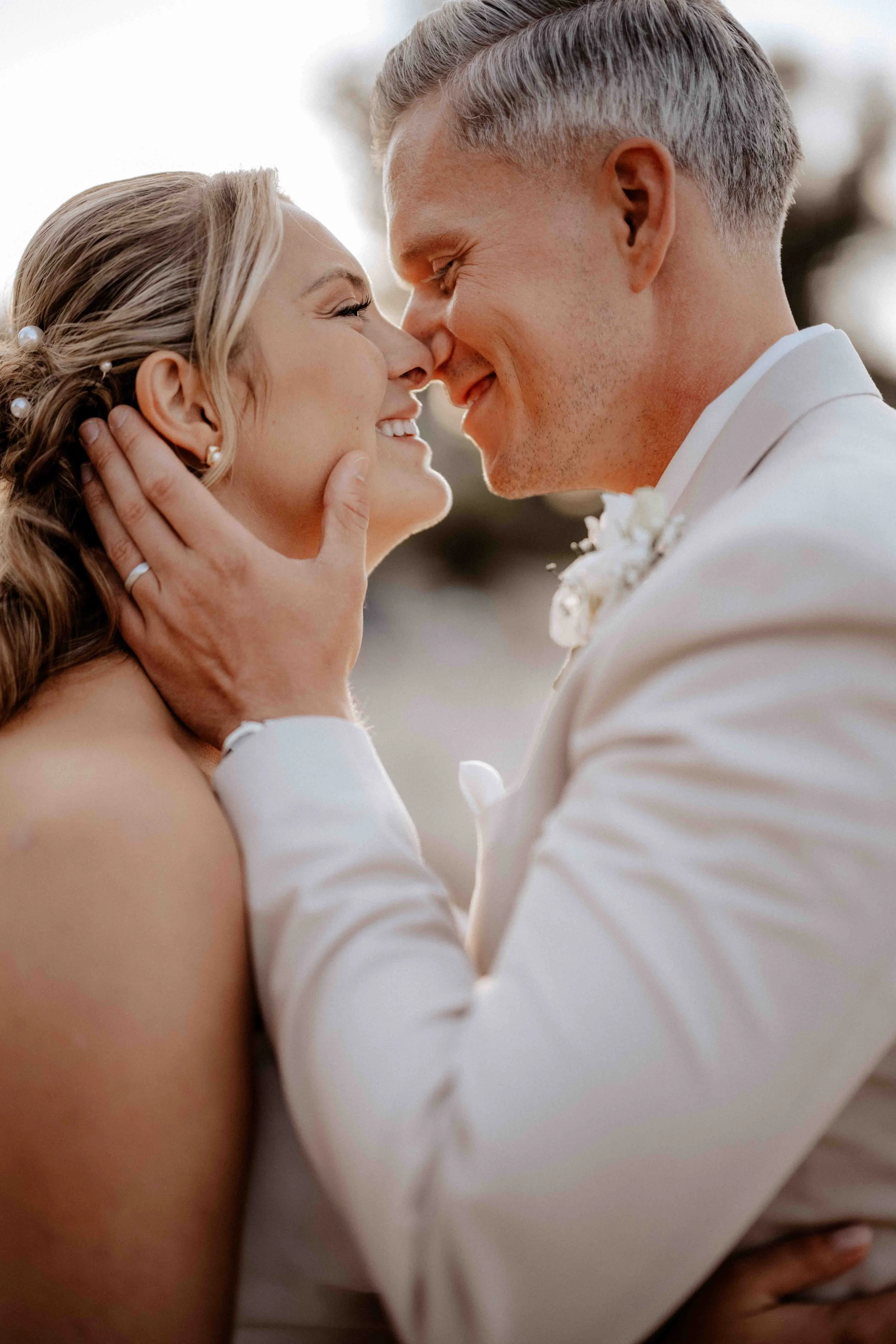 Ein glückliches Brautpaar bei einer Hochzeit, sie lächeln sich an und berühren sich an den Nasen, umarmt von Liebe. Die Hochzeit findet in Köln Rodenkirchen am Rhein im Strandschlösschen statt. 